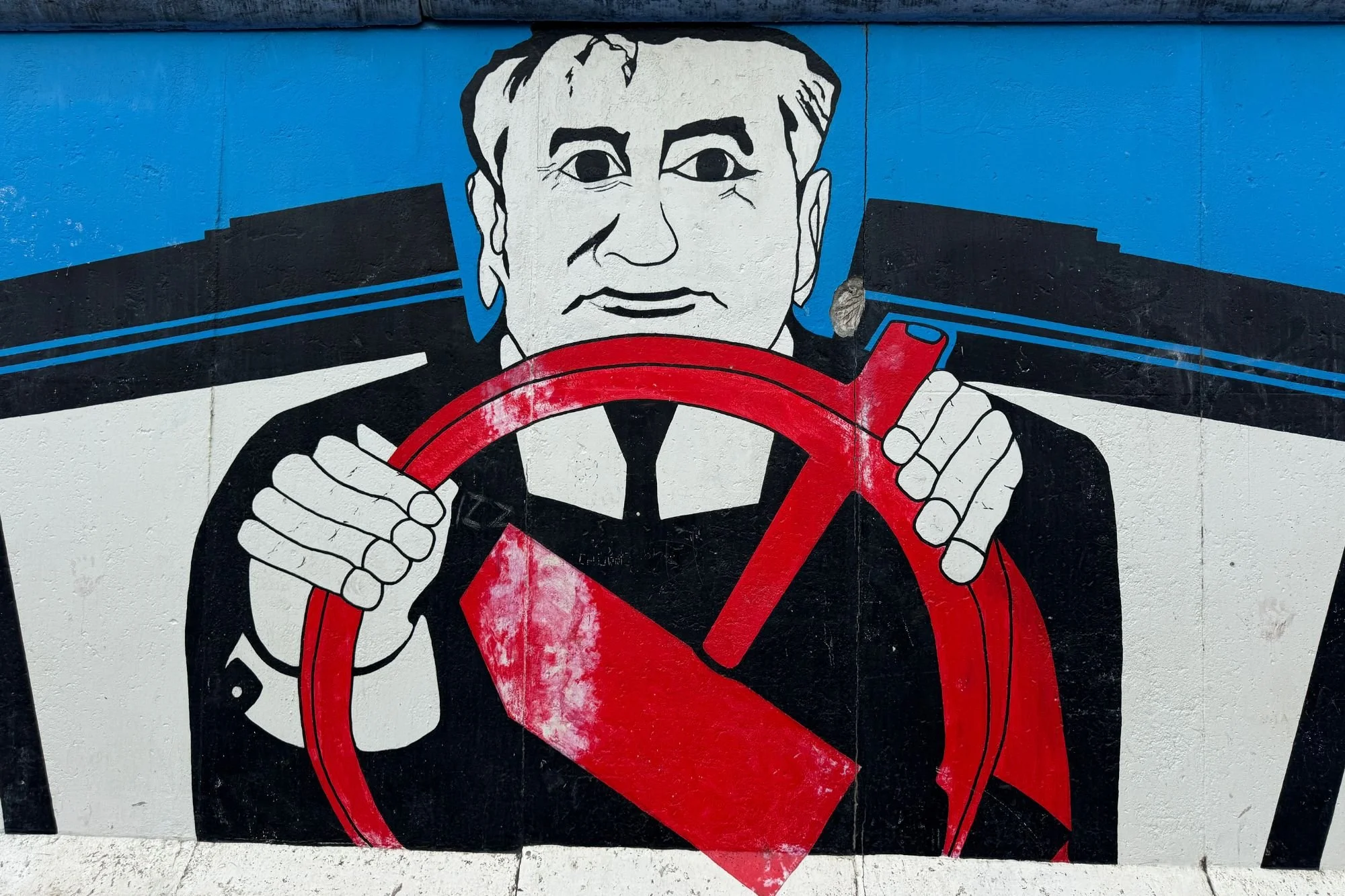 The Gorbachev Hammer and Sickle mural by Dmitri Vrubel on the Berlin Wall, featuring Soviet leader Mikhail Gorbachev gripping a red steering wheel.