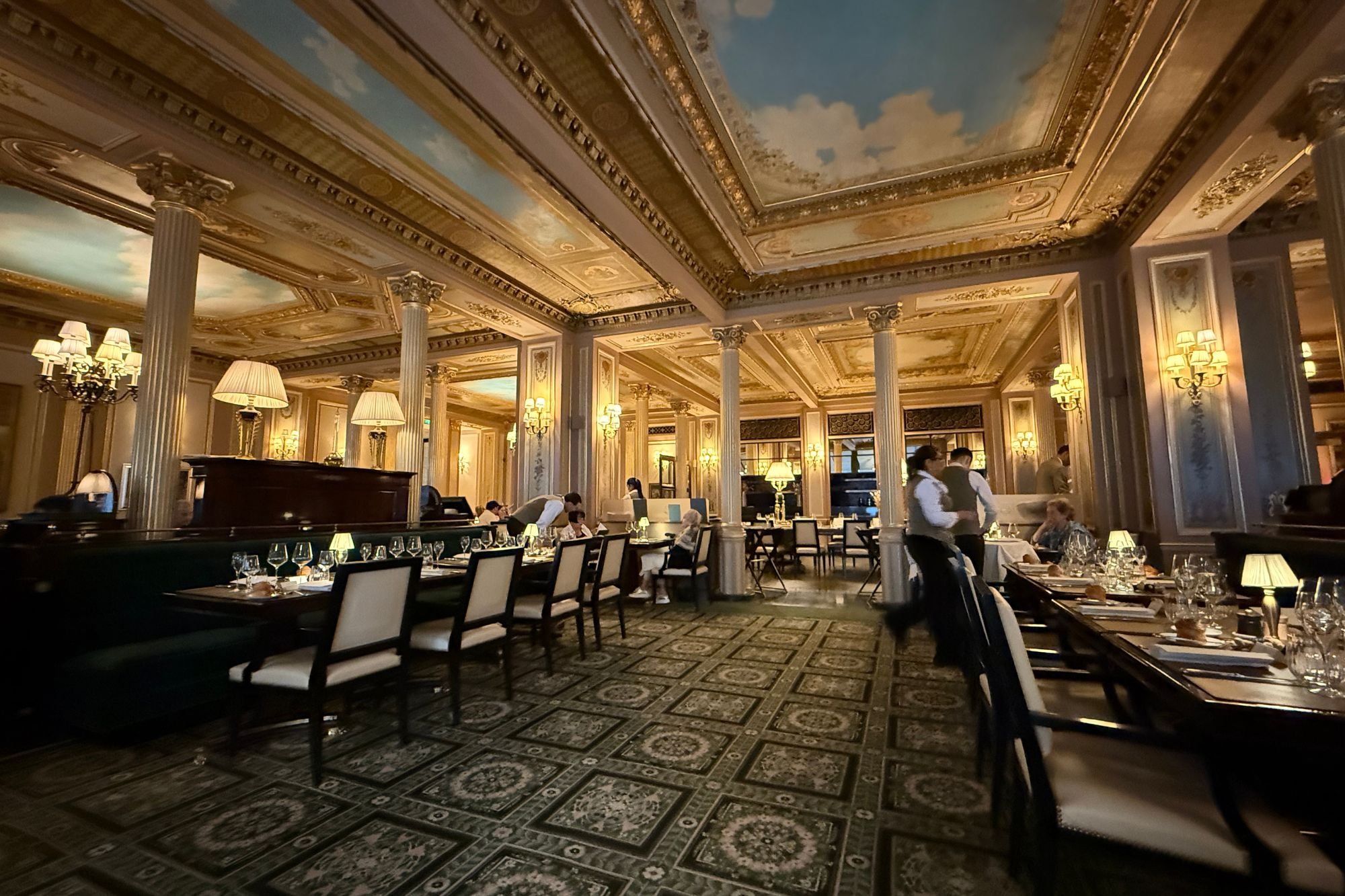 The grand Napoleon III dining room at Café de la Paix Paris featuring painted ceiling frescoes, gilded columns, and set tables