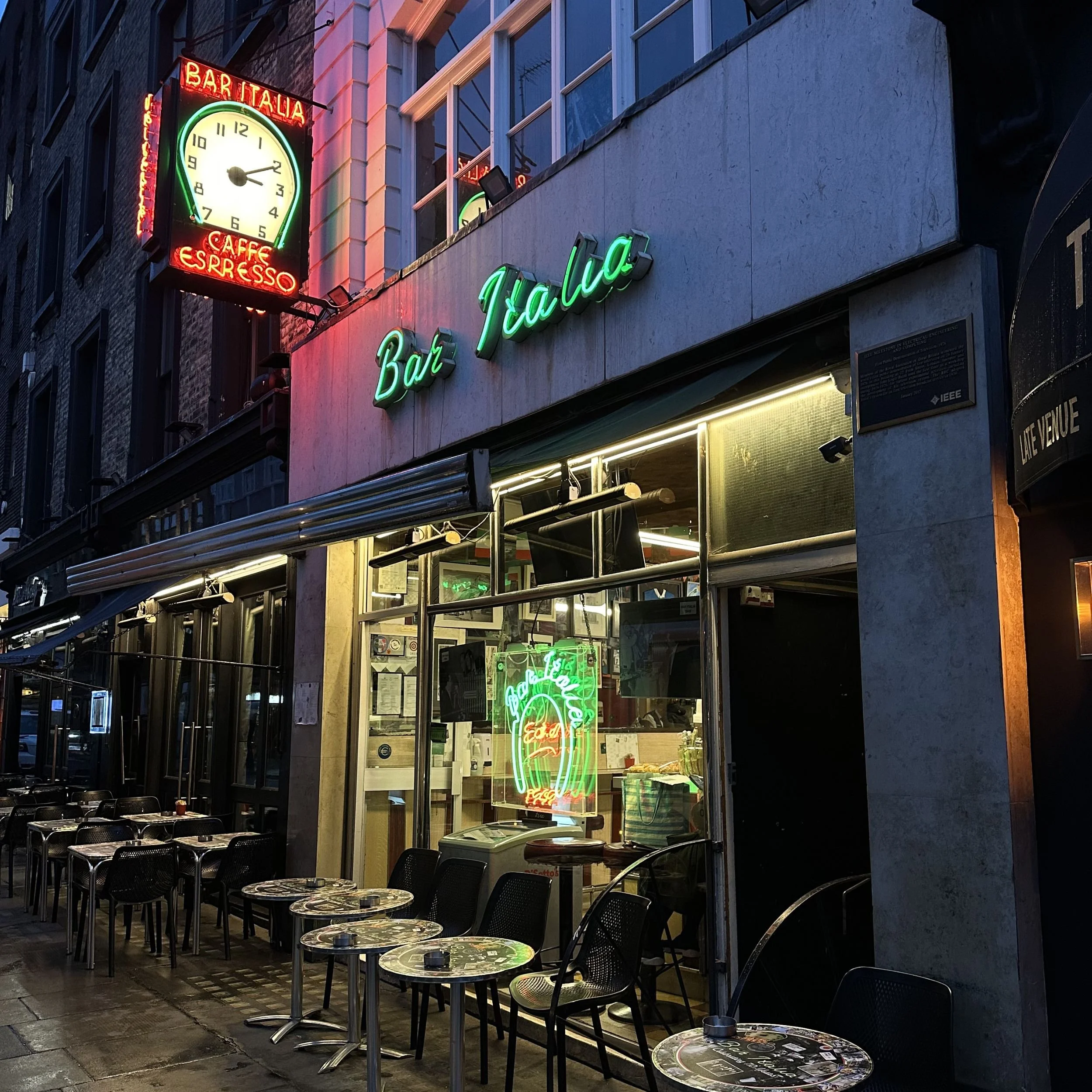 Exterior of Bar Italia at dusk in the rain with the red and green clock and neon sign