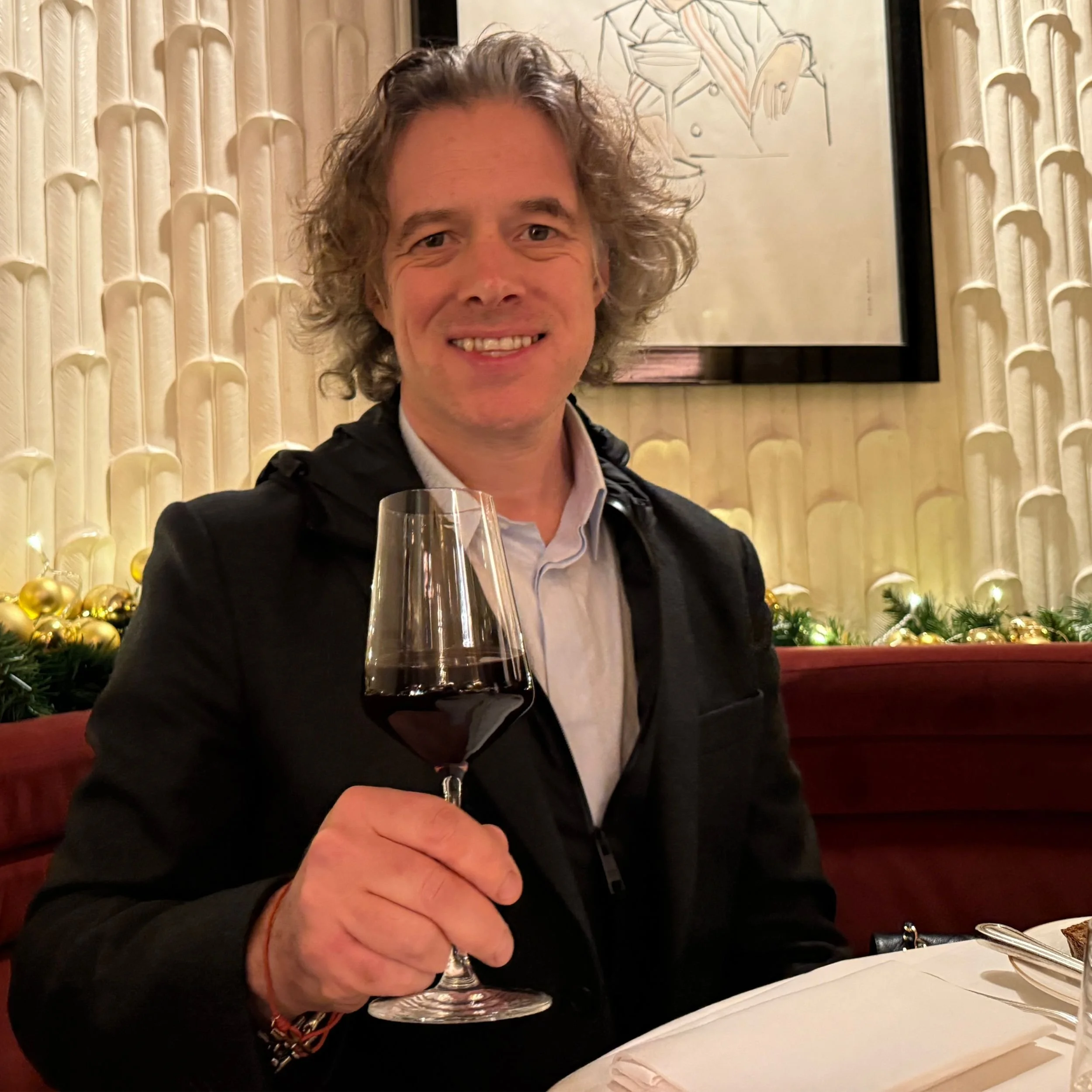Jamie Riddell pictured at the Savoy Grill smiling with a large glass of red wine held up