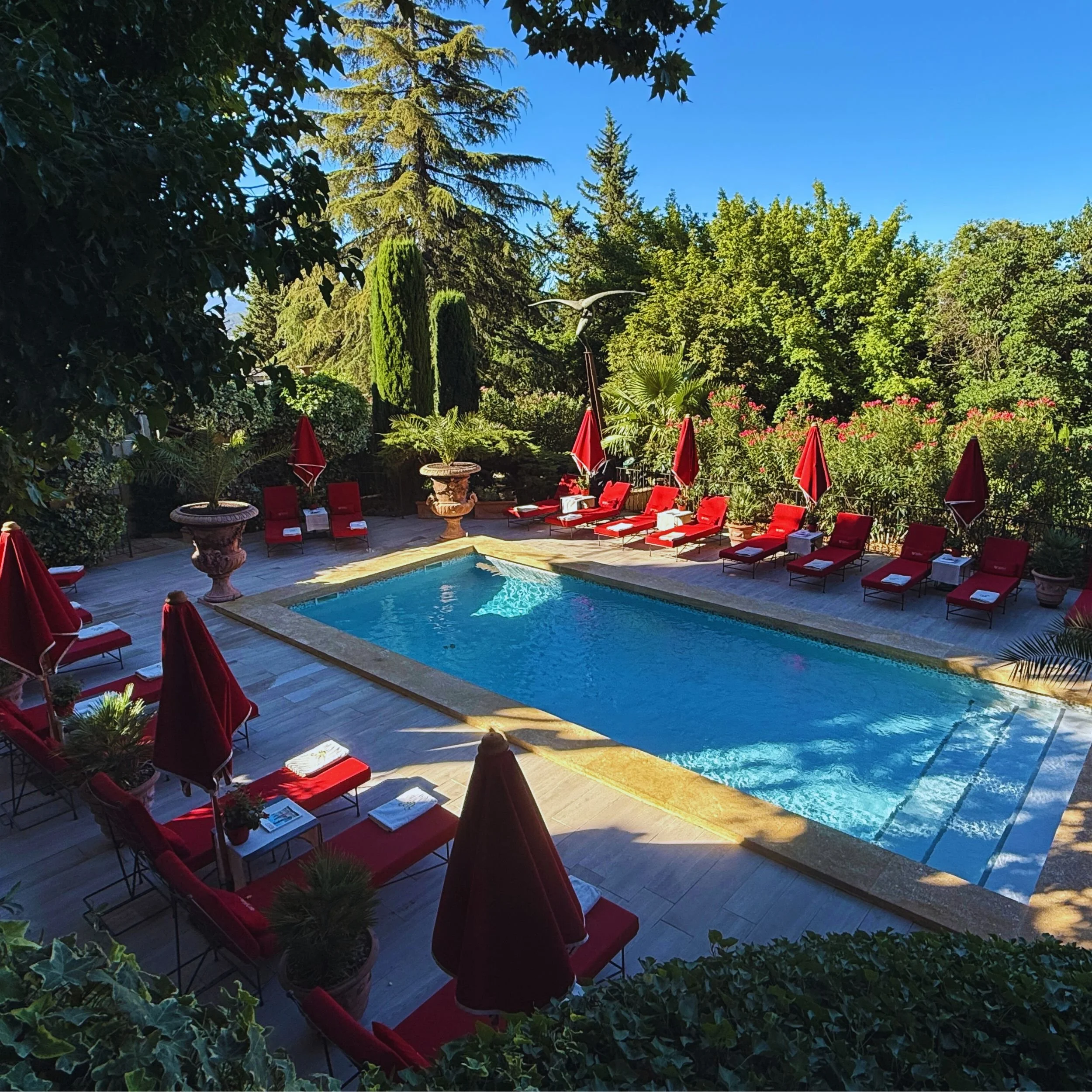 Villa Gallici swimming pool with red loungers and parasols set within the hotel gardens in Aix-en-Provence