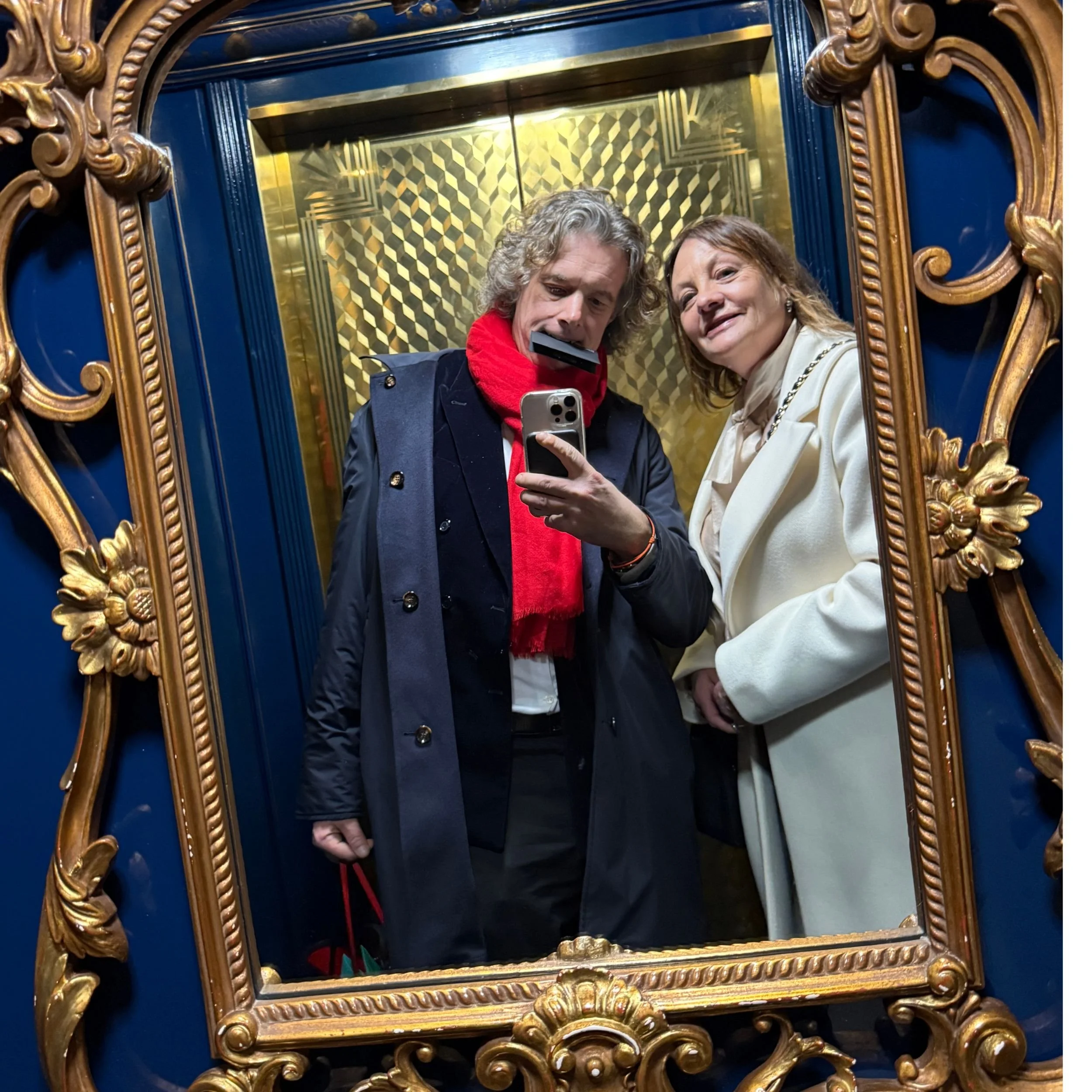 Jamie and Katherine photographed in the gold framed mirror against the dark blue interior of the Blue lift at the Savoy