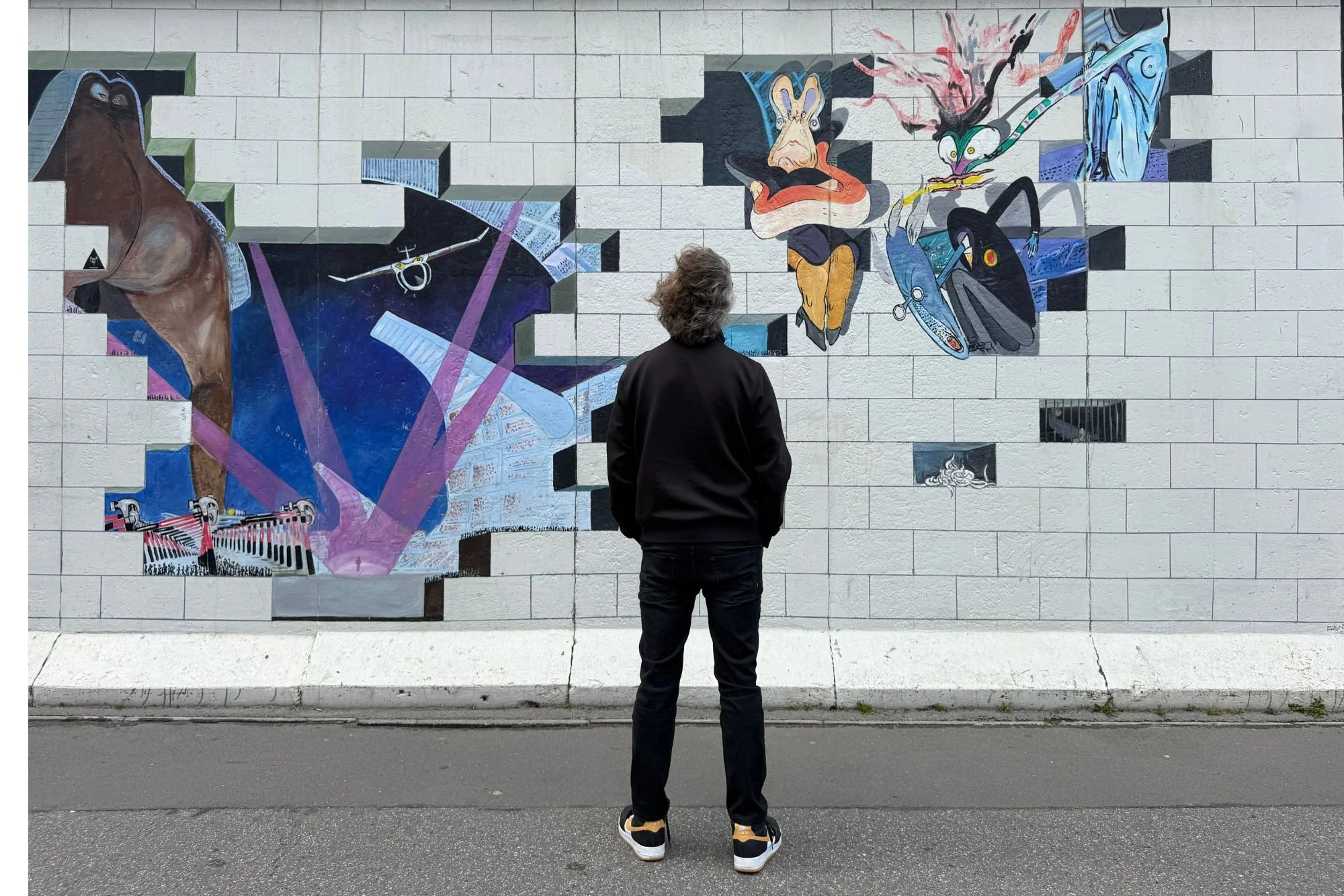 Jay viewing the Pink Floyd The Wall mural at the East Side Gallery, showing the distinctive white brickwork and surreal cut-out design.
