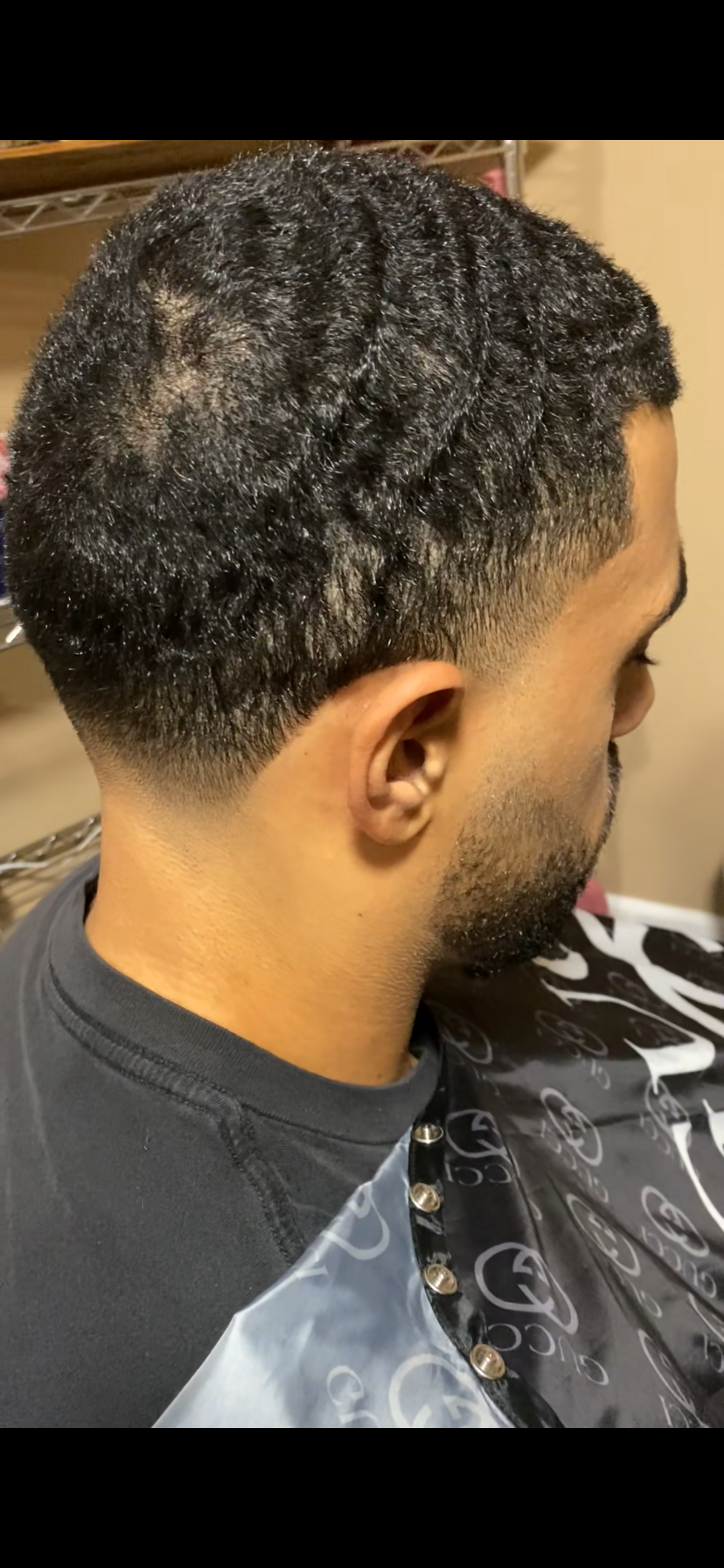 A man with a fade haircut and tightly textured curly hair on top, sitting in a barber's chair.