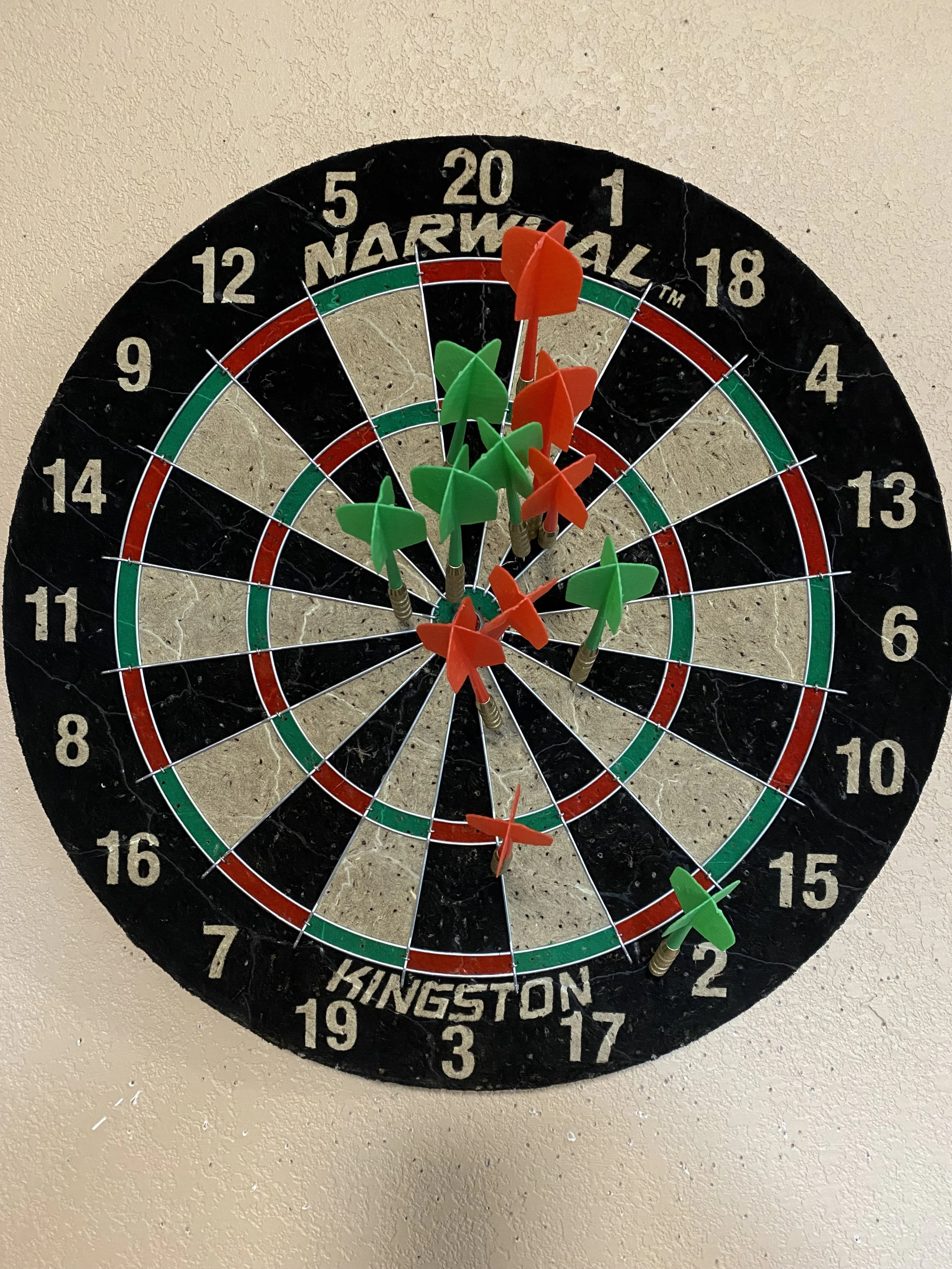Dartboard with numerous red and green darts stuck in it.