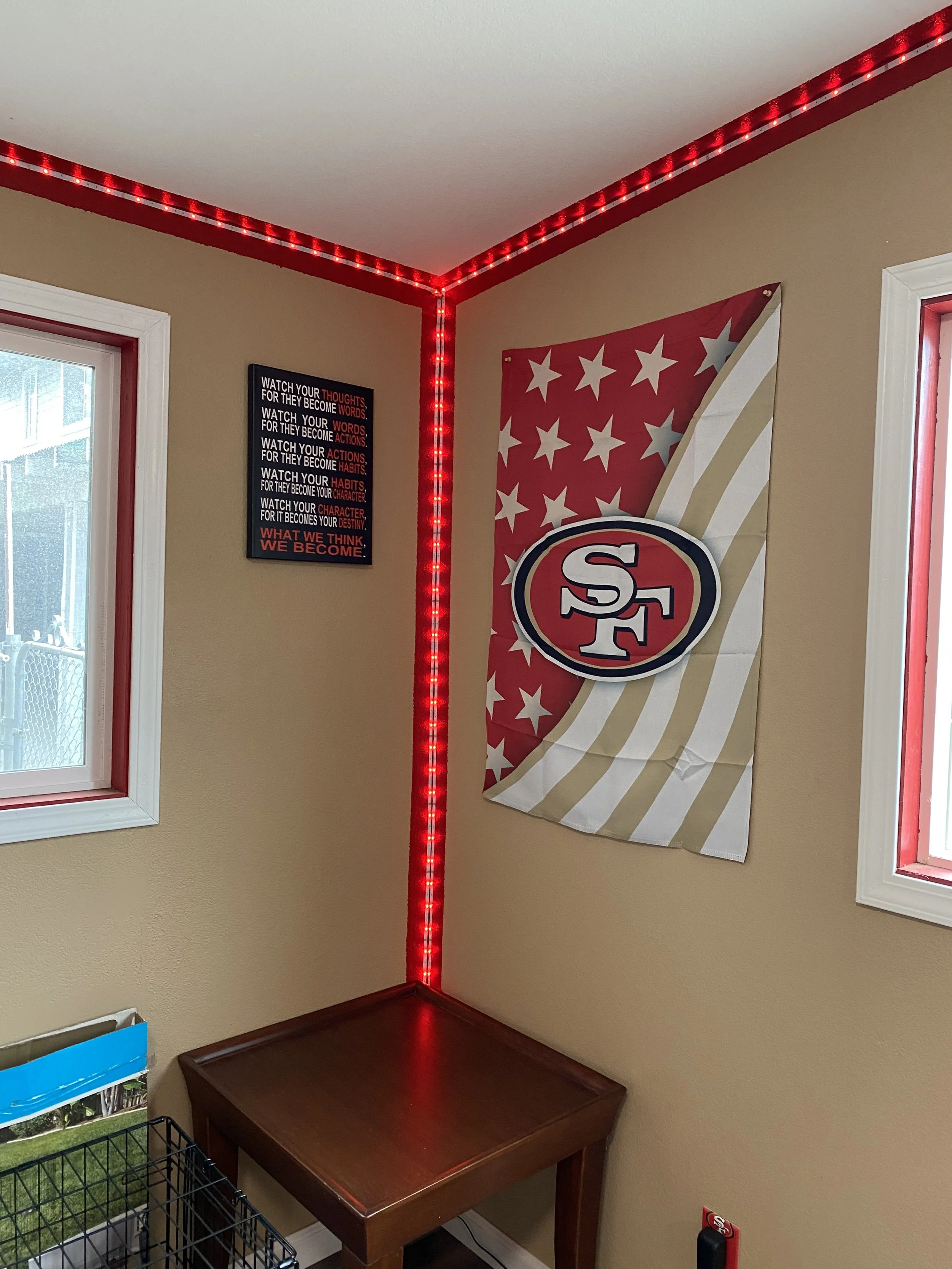 Corner of a room with a San Francisco 49ers flag, a motivational poster, and red LED strip lighting along the ceiling corner.