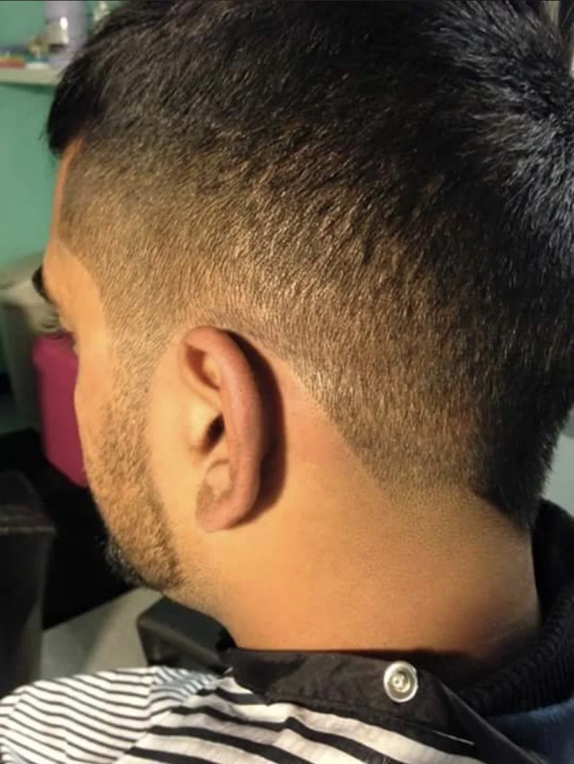 Close-up of a man's head showing a fresh, short fade haircut with tapered sides and back, and longer hair on top.