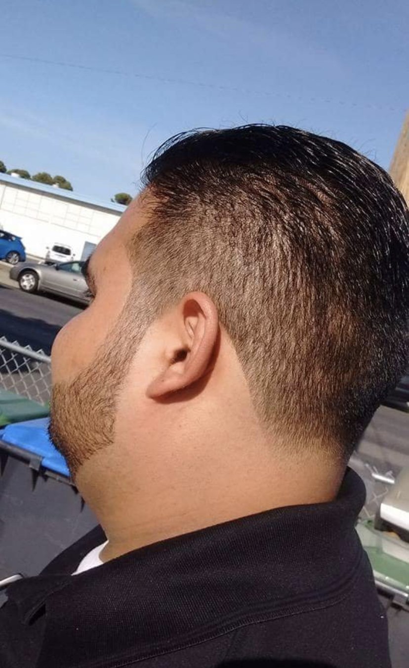 Close-up of a man with a short fade haircut, dark hair on top styled back, and clean-shaven face, outdoors in a parking lot.