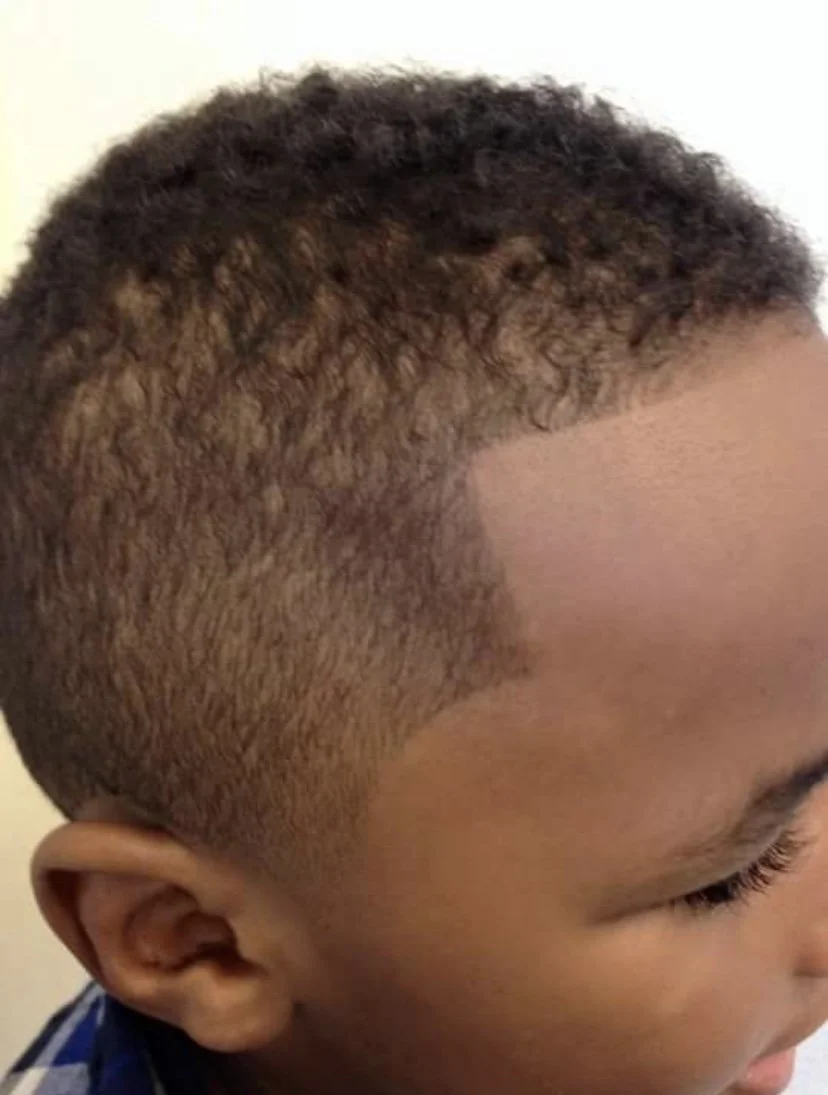 Close-up of a child's head with a modern fade hairstyle featuring curly hair on top and shaved sides.
