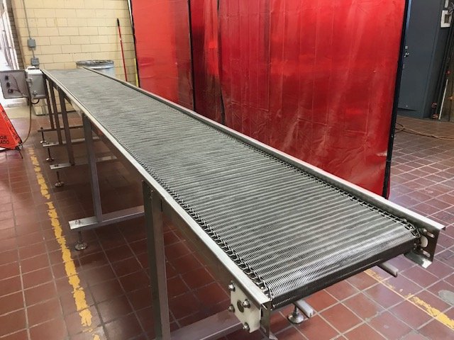 An industrial conveyor belt in a workshop with red and beige walls, metal flooring, and a red partition.