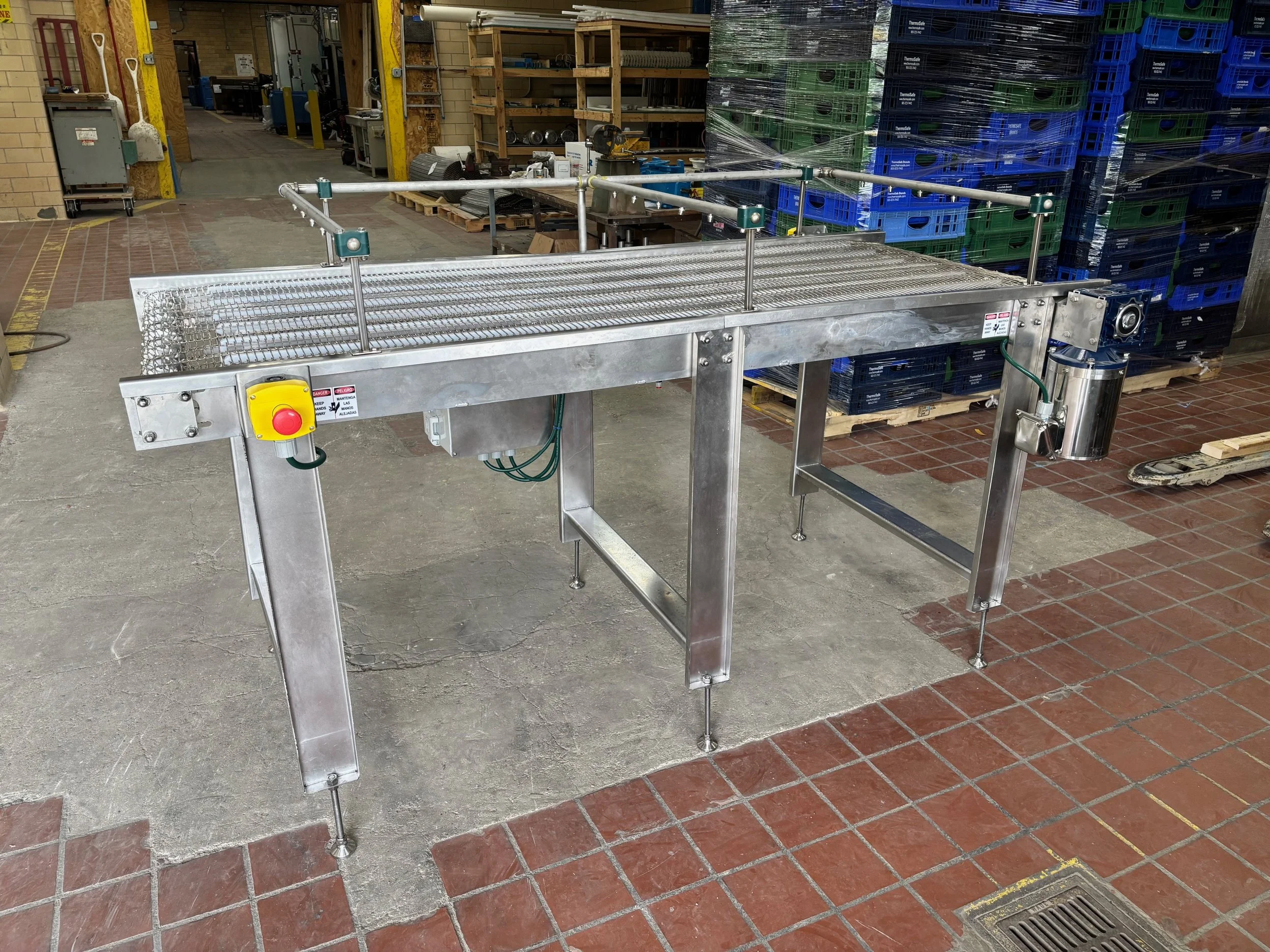 Stainless steel industrial conveyor with safety railings in a warehouse.