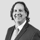 Black and white photo of a man with shoulder-length hair, wearing a suit and tie, smiling.
