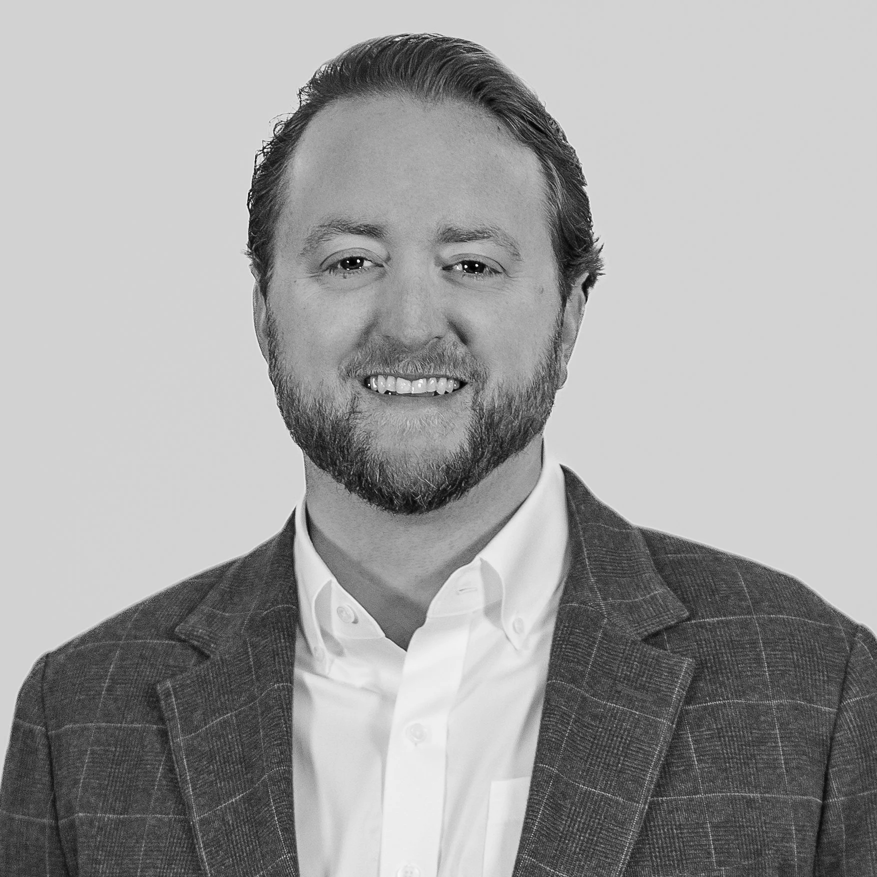 Black and white headshot of a smiling man with a beard, wearing a suit jacket and white shirt.