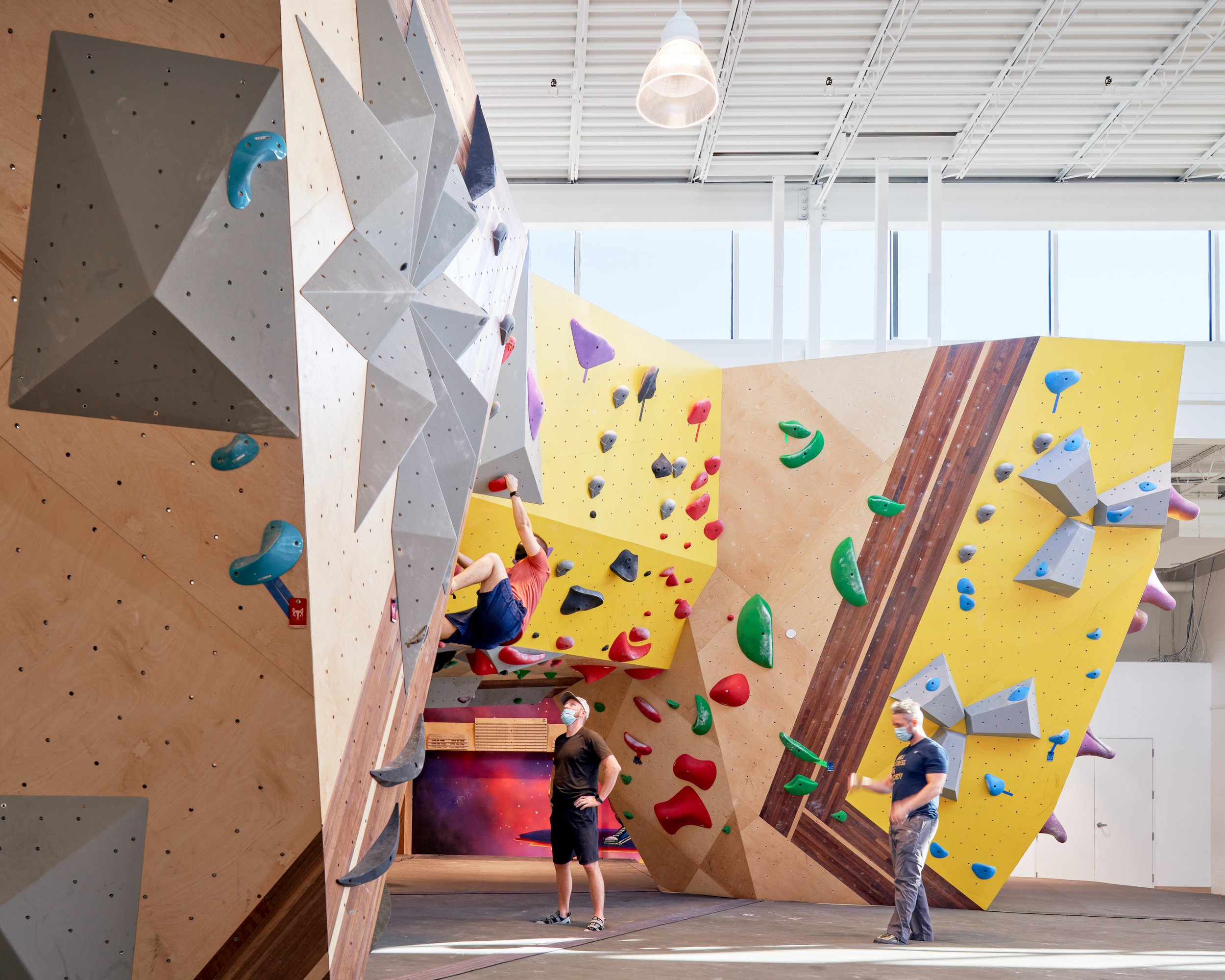 Angular climbing walls framed in color-blocked panels showcase the sculptural clarity of the space. A compass rose motif and integrated lighting emphasize form, movement, and graphic identity.