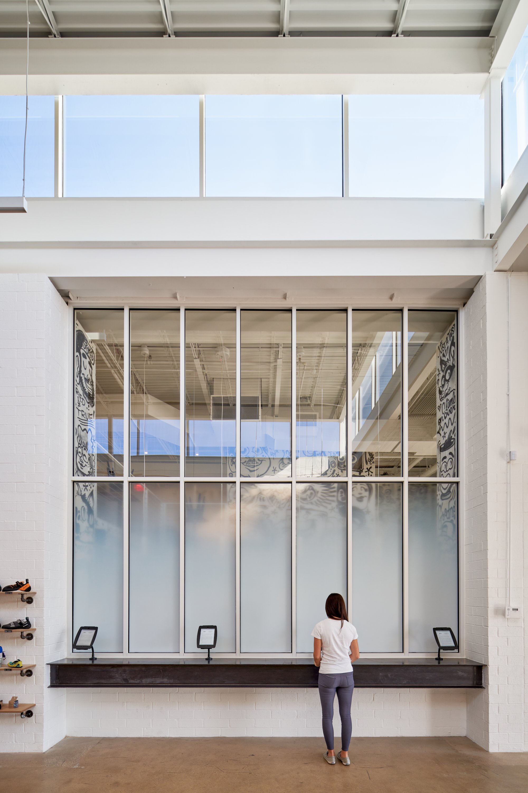 This custom steel and glass installation allows for natural daylight to enter while maintaining privacy for the coffee shop. A built-in steel counter provides check-in access, framed by a clean white brick backdrop.