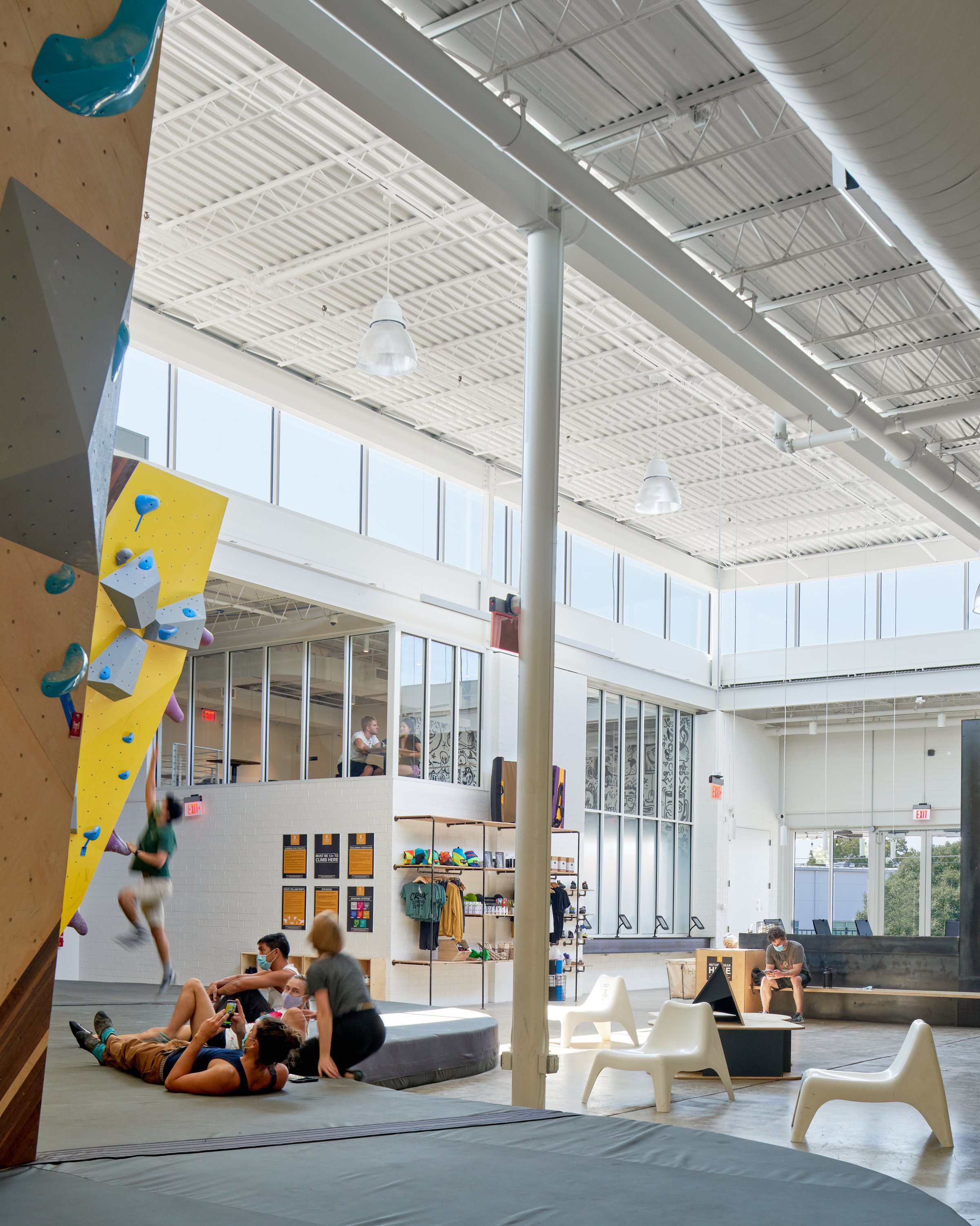 A sunlit corner of the facility reveals the retail zone and a glass-wrapped coffee mezzanine. Translucent panels and clerestory glazing allow for privacy without losing daylight.