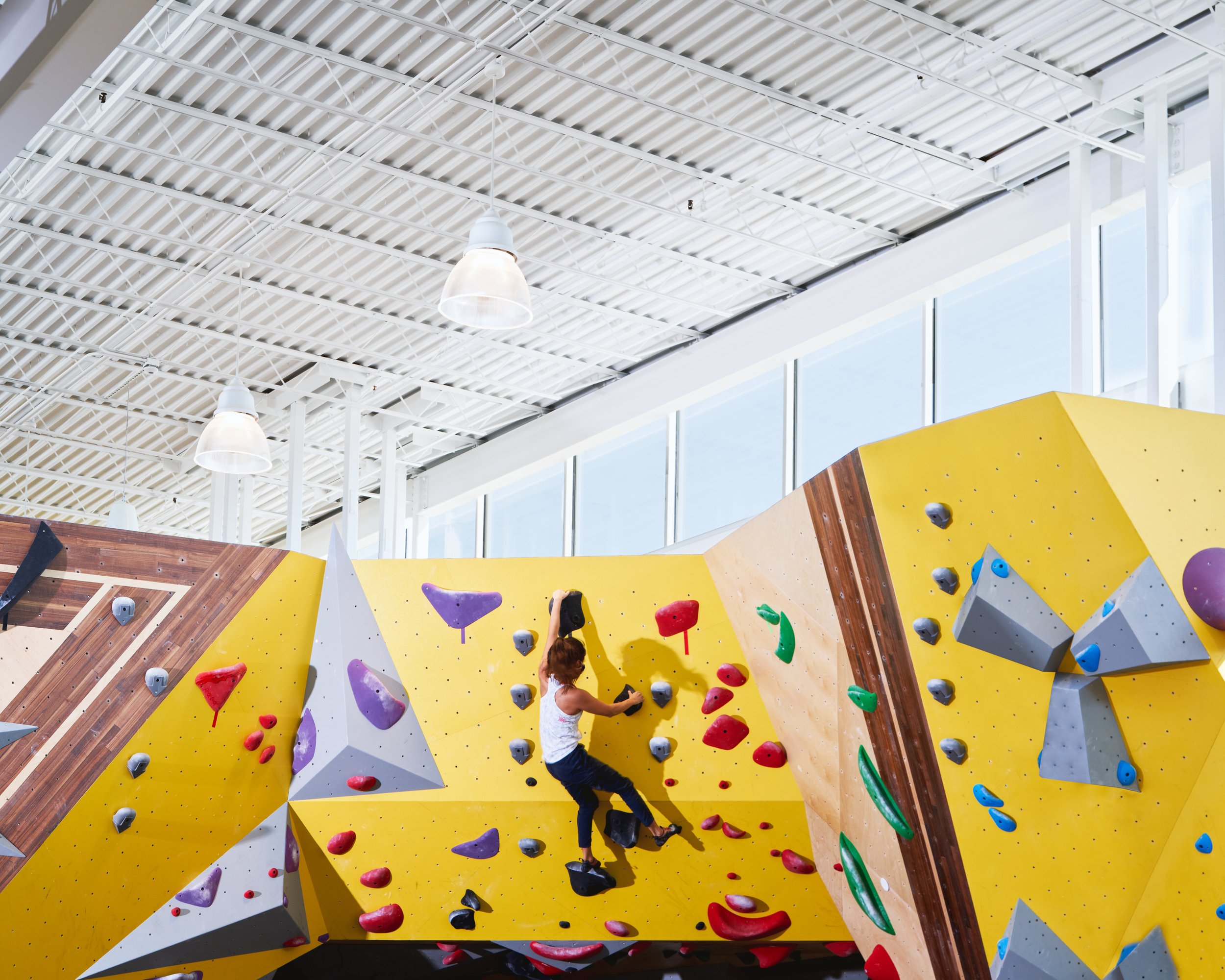 This shot highlights how carefully placed skylights and clerestory windows wash the bouldering walls in natural light, enhancing color contrast and supporting an energizing indoor experience.