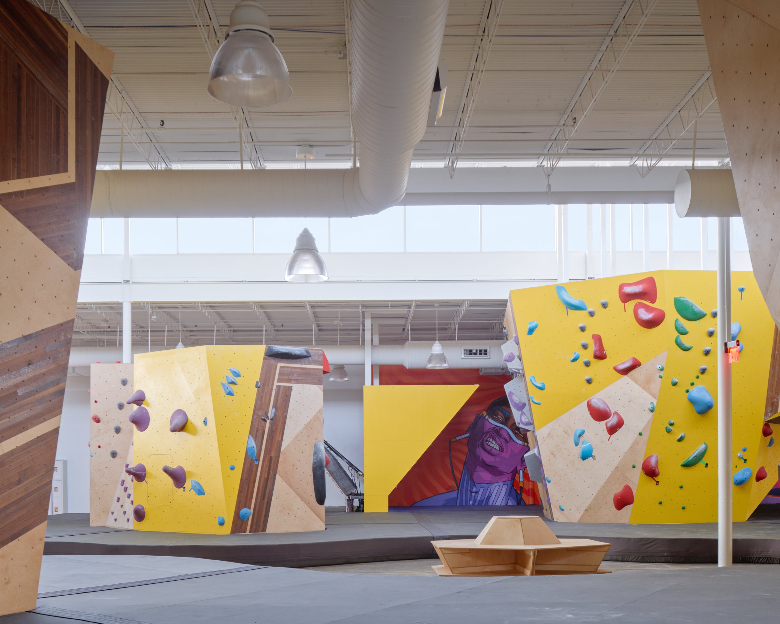 A head-on view showcases the rhythmic geometry of the climbing terrain, anchored by a bold mural and sculptural seating. Natural light and graphic color keep the open space vibrant and alive.