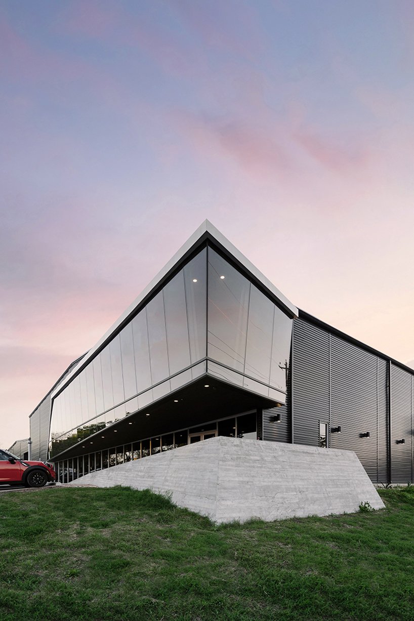 A faceted glass volume lifts above black metal siding, marking the transformation from auto shop to climbing gym and framing views from the elevated yoga studio.
