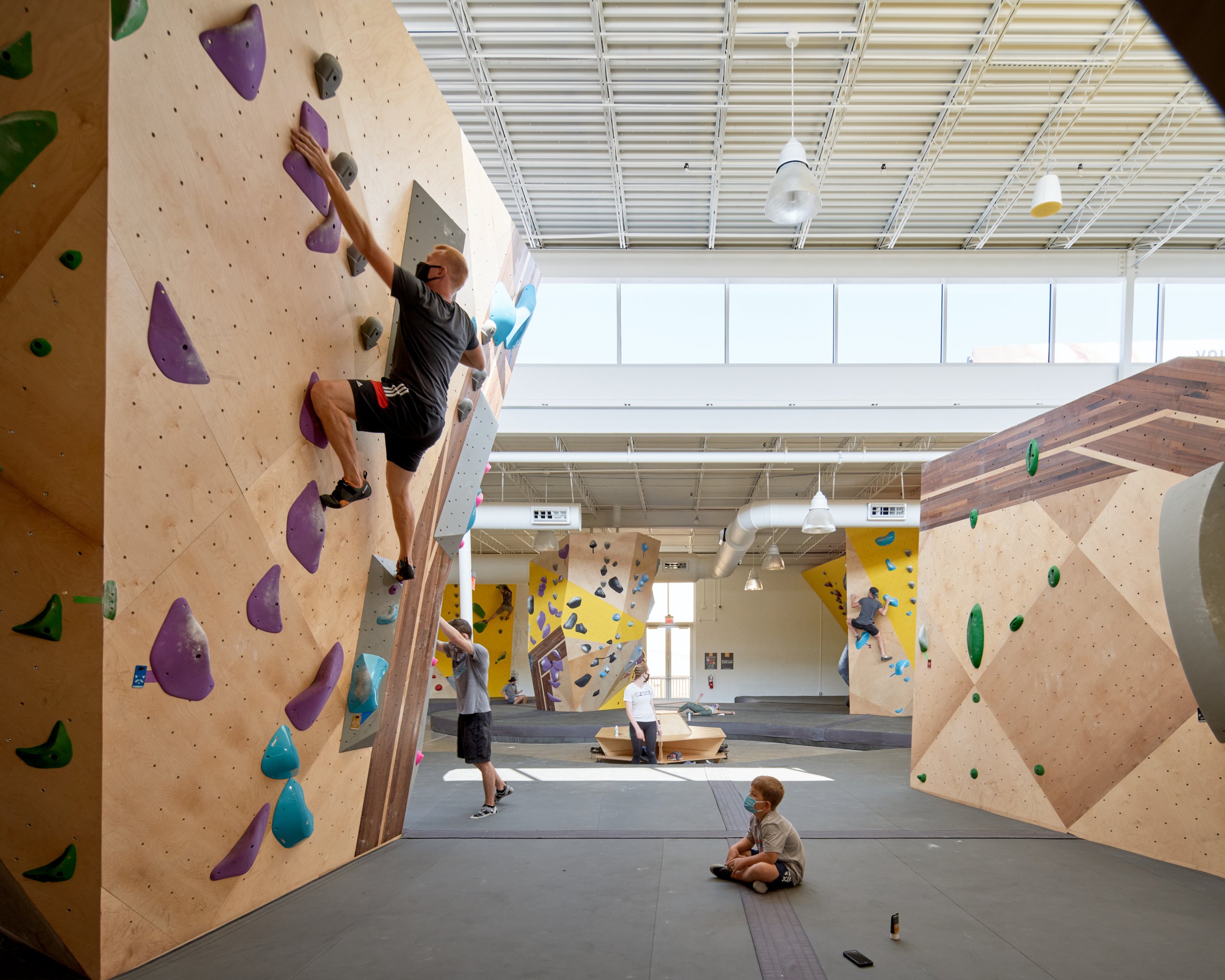 This image captures the multi-generational spirit of Crux Central, where climbers and spectators—kids and grownups—share a light-filled space shaped by crisp geometry and calm material tones.