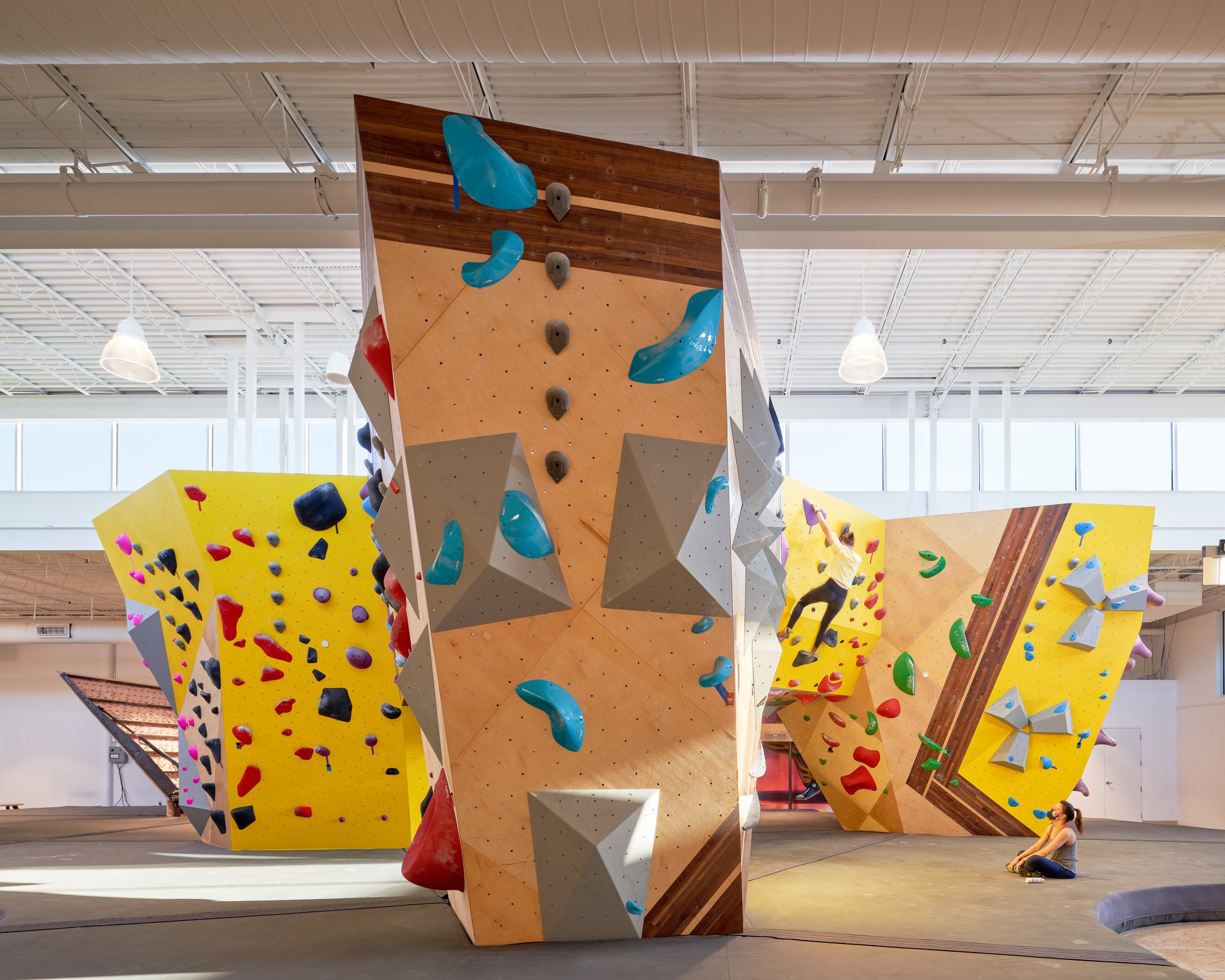 This view centers on the vertical centerpiece—a freestanding climbing monolith that anchors the gym. Its faceted geometry, layered textures, and custom hold layouts create both visual interest and climbing challenge.