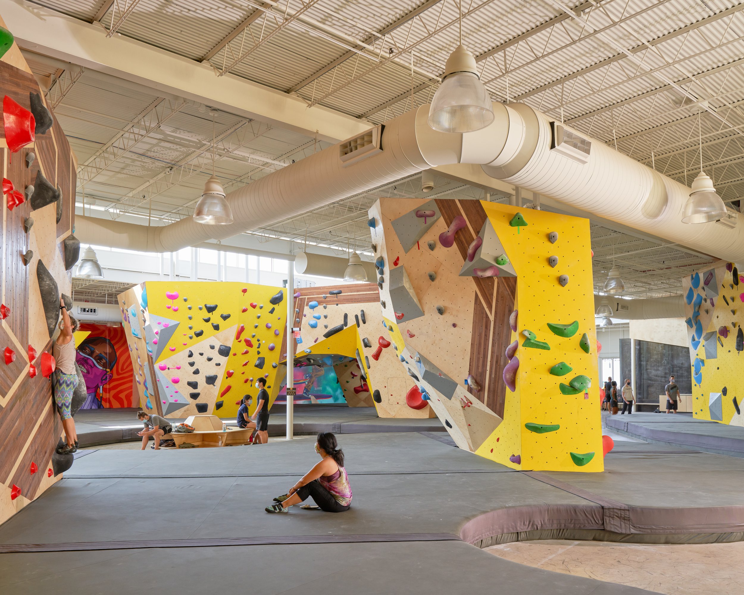 This image highlights the variety of wall forms and climbing surfaces at Crux Central, framed by exposed ductwork and clerestory daylight that amplify the industrial character of the space.