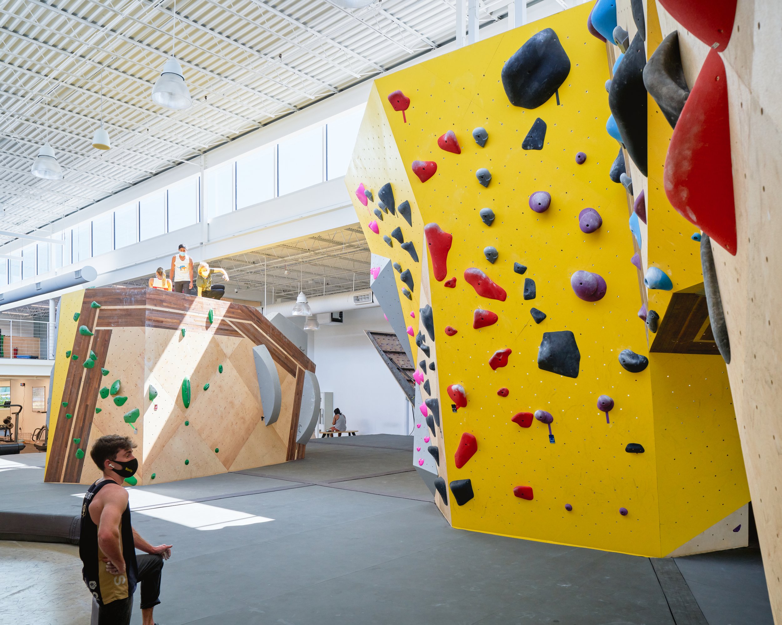 A view down the main climbing corridor reveals wall diversity—from slab to overhang—framed by clerestory light and moments of rest, reflection, and social interaction.