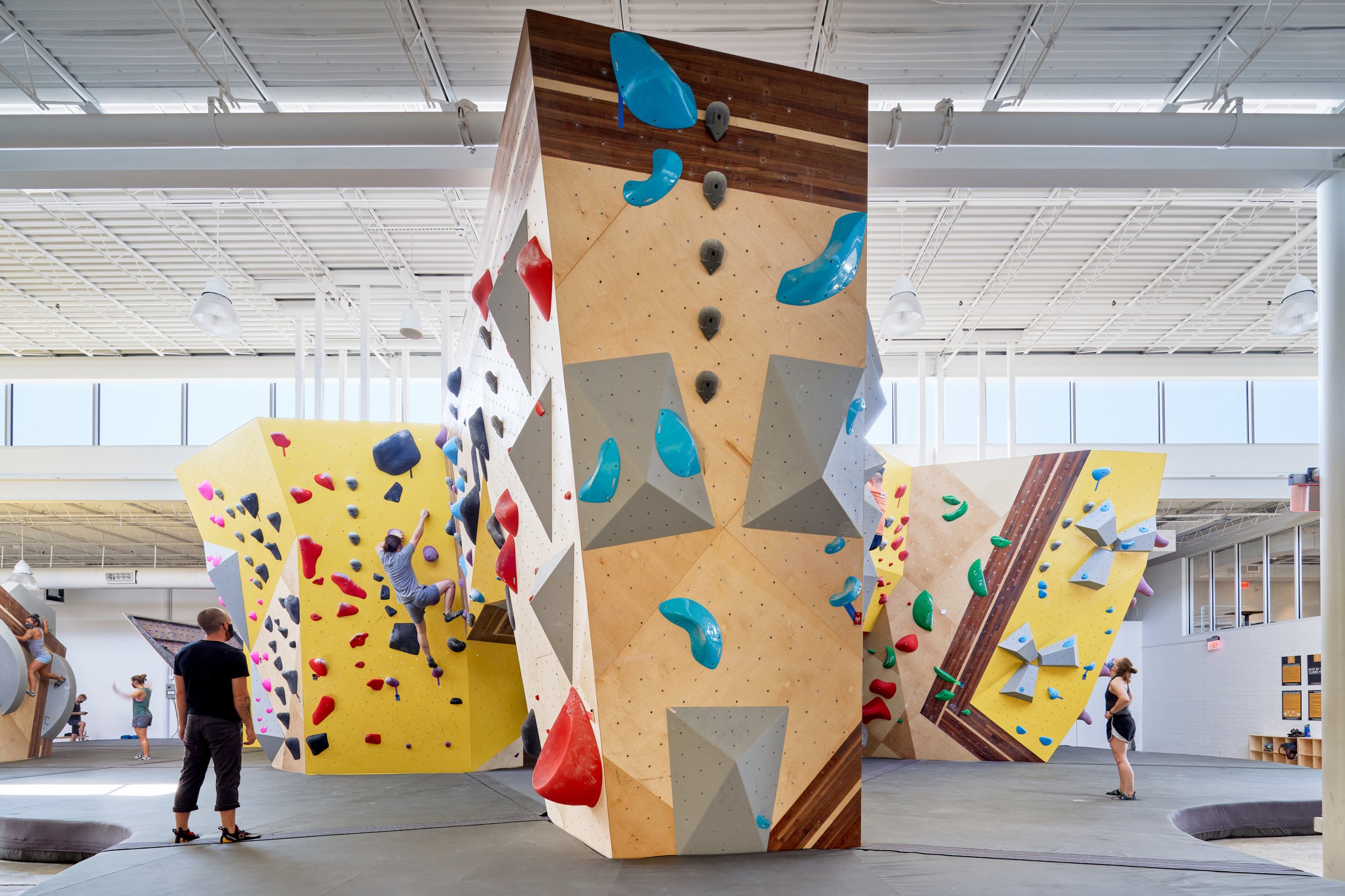 This head-on view emphasizes the faceted form and layered material palette of Crux Central’s climbing centerpiece—both architectural landmark and athletic challenge.