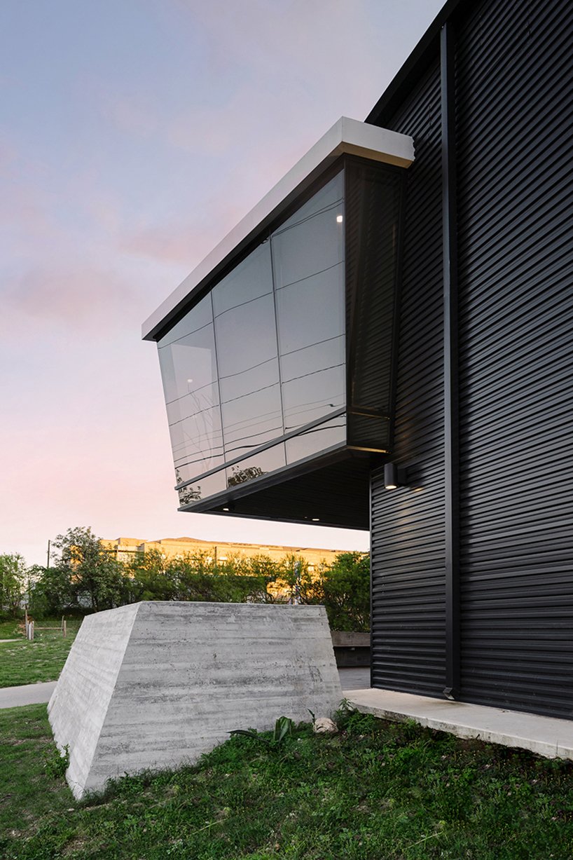 The angular glass volume projects from the original warehouse, anchored by board-formed concrete that recalls the site's gritty past while elevating its new identity.