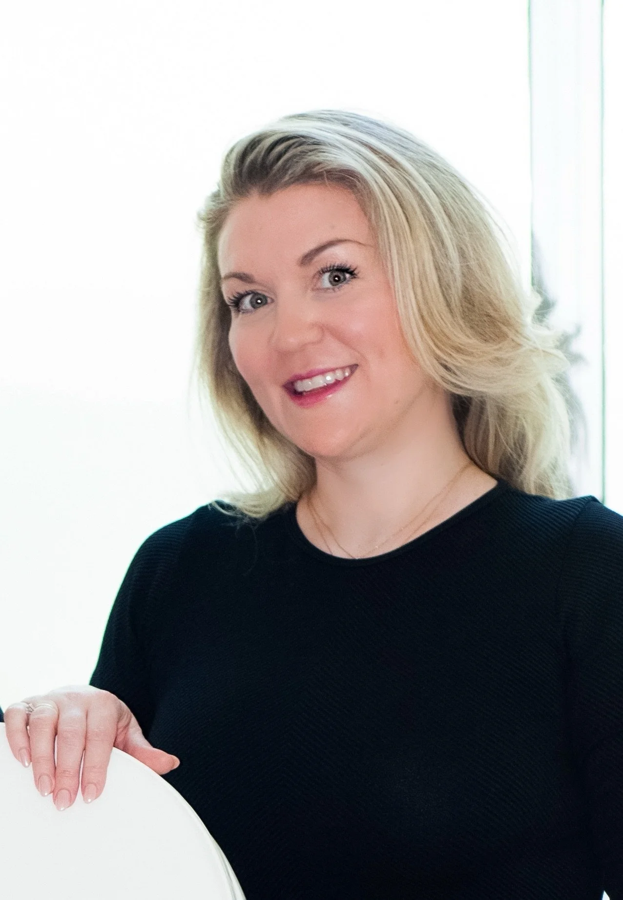A woman from Valere Medical Aesthetics with blonde hair smiling, wearing a black top, against a light background.