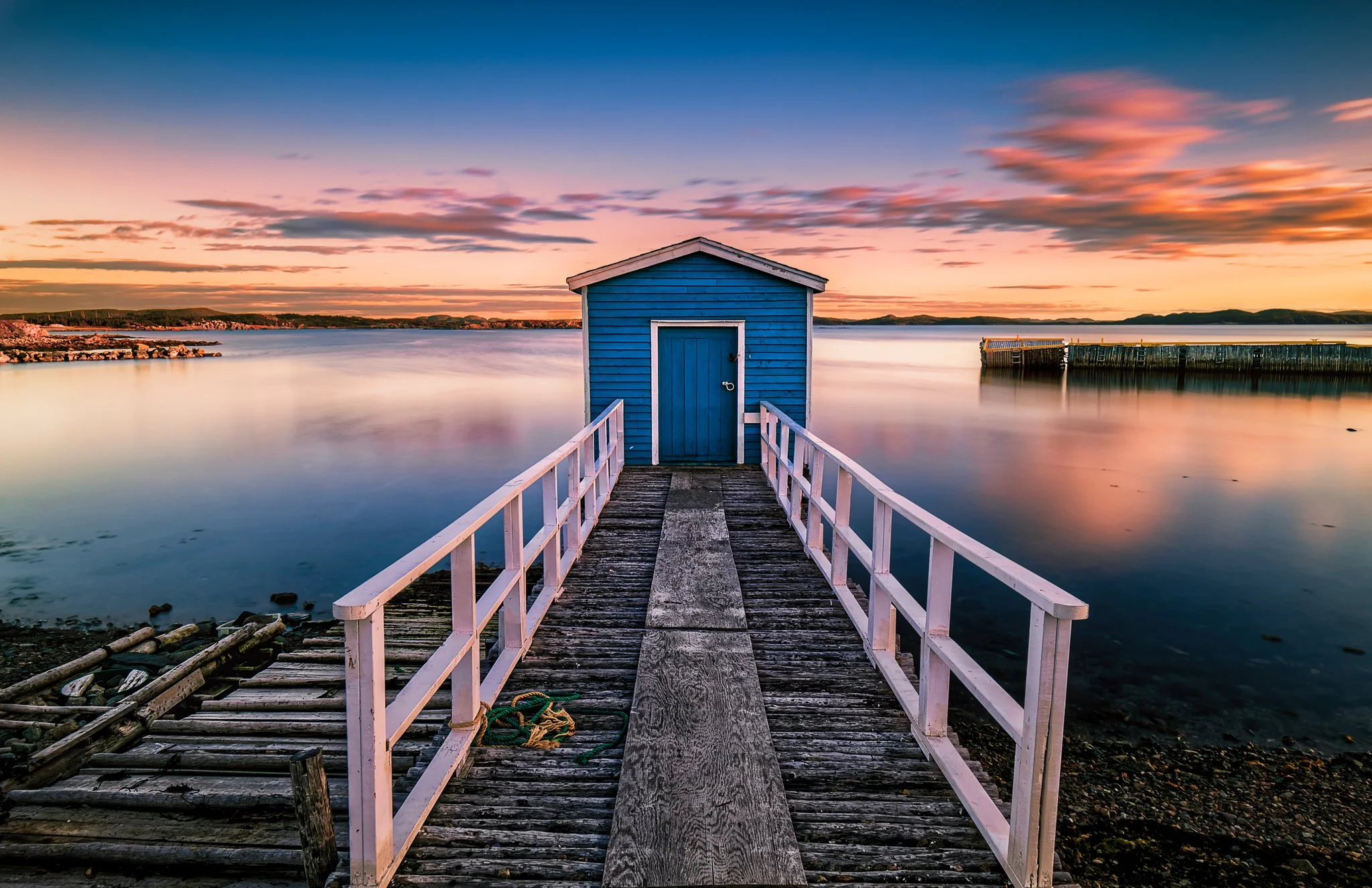 A quiet evening at Twillingate Island as the light settles over the water.  his blue fishing stage sits at the end of a weathered wharf, with calm water reflecting the last colours of the day.