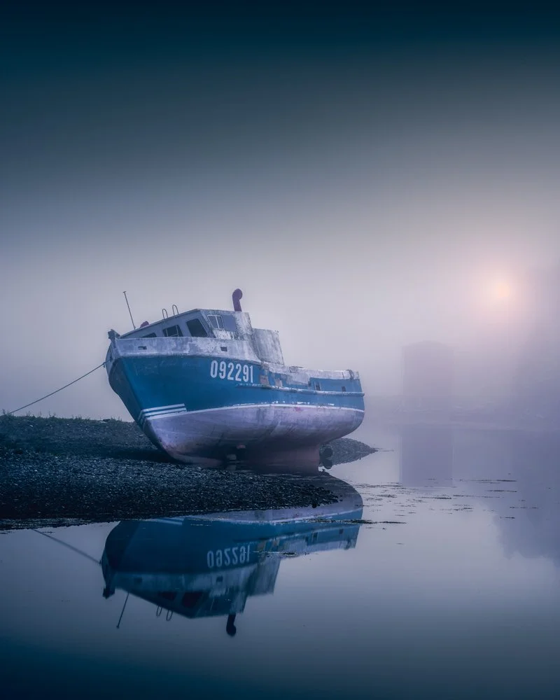 A boat sits along the shore on a foggy morning at Port au Bras Newfoundland.