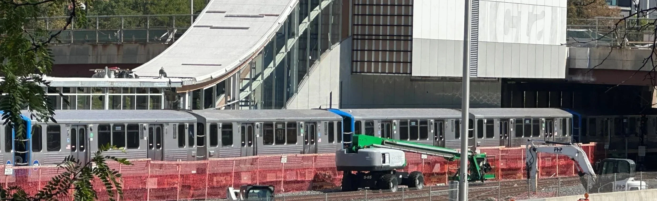 Train stopped at CTA Blue Line Racine station's new entrance seen from the south, with some construction netting up around the track.