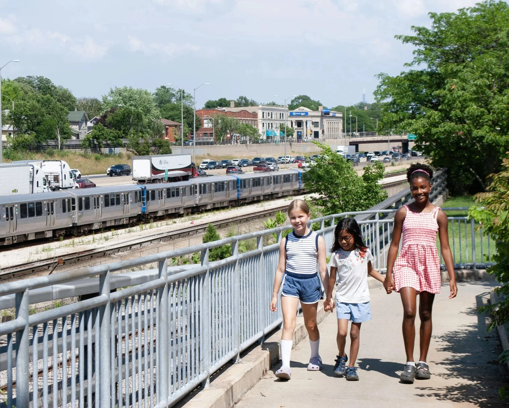 Children approach accessible pedestrian bridge in Oak Park walk Interstate 290 and a Forest Park bound CTA Blue Line train.