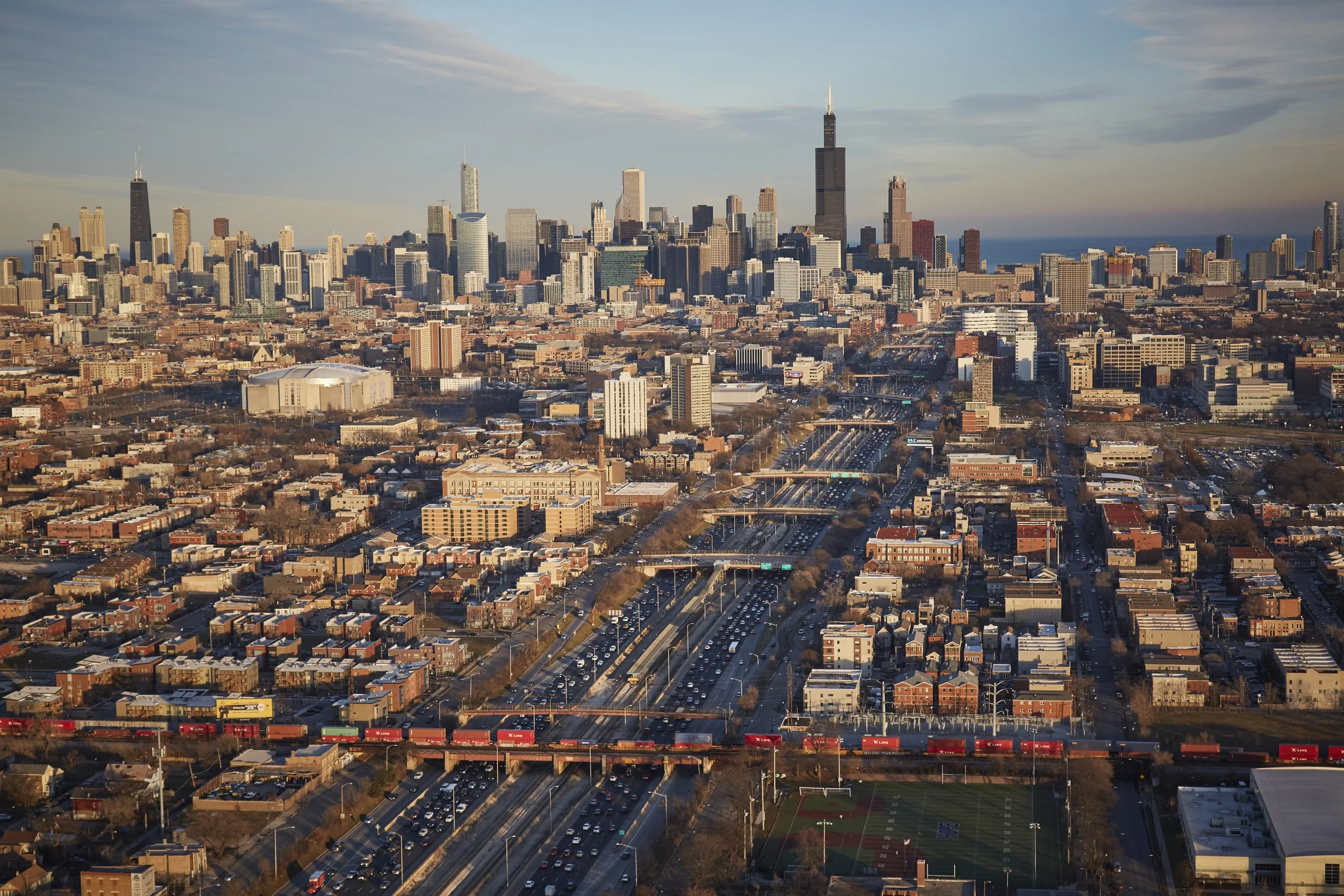 Aerial view of Chicago looking east toward downtown from California Ave, showing city skyline, freight train on Union Pacific rail, and multiple bridges over I-290