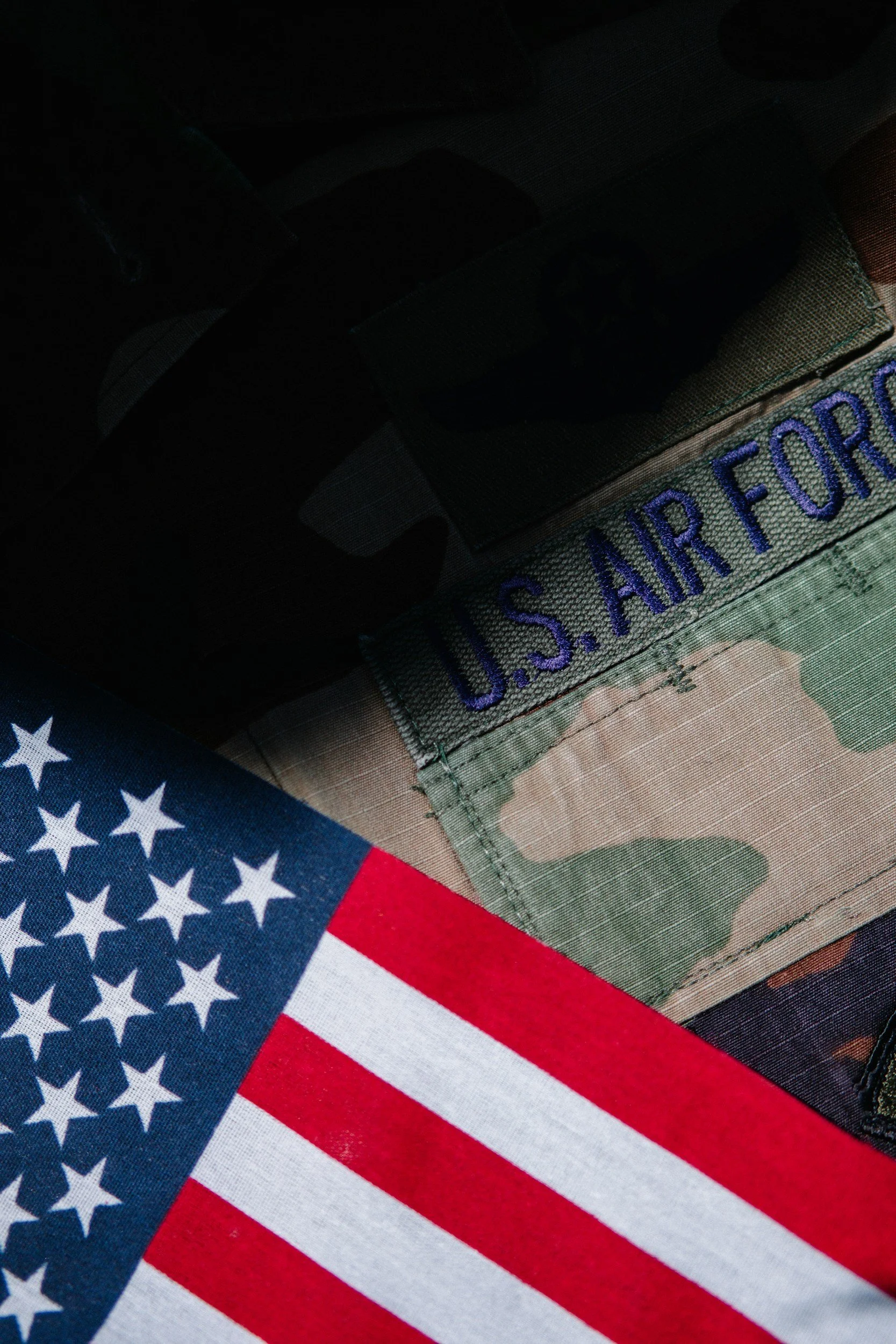 Close-up of an American flag and a U.S. Air Force patch on camouflage fabric, possibly part of a military uniform.