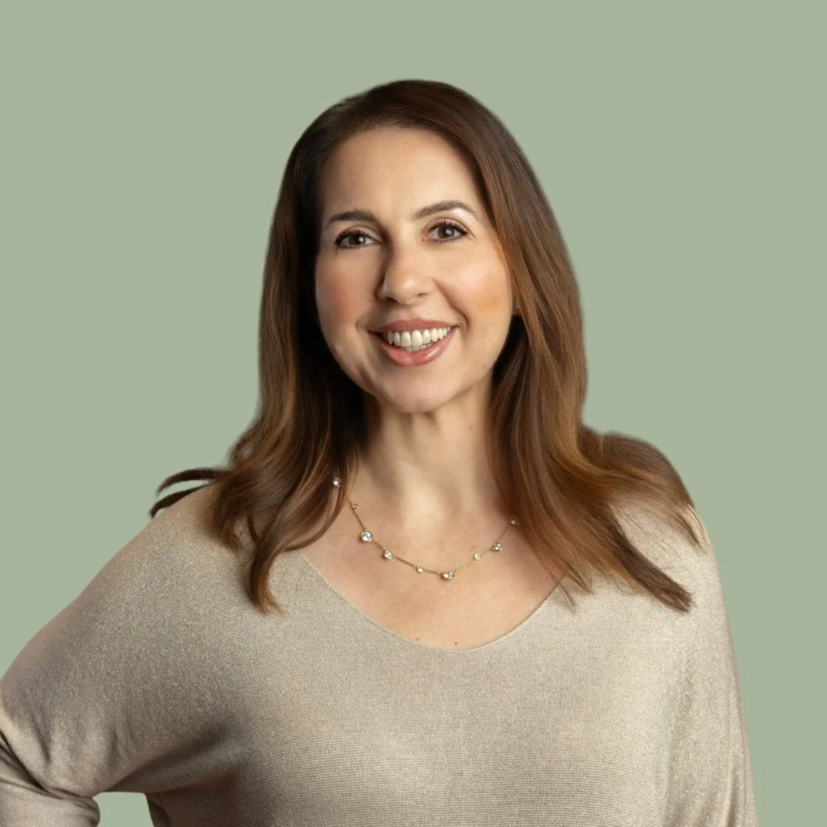 A woman with brown hair smiling, wearing a beige top and a necklace, against a light green background.