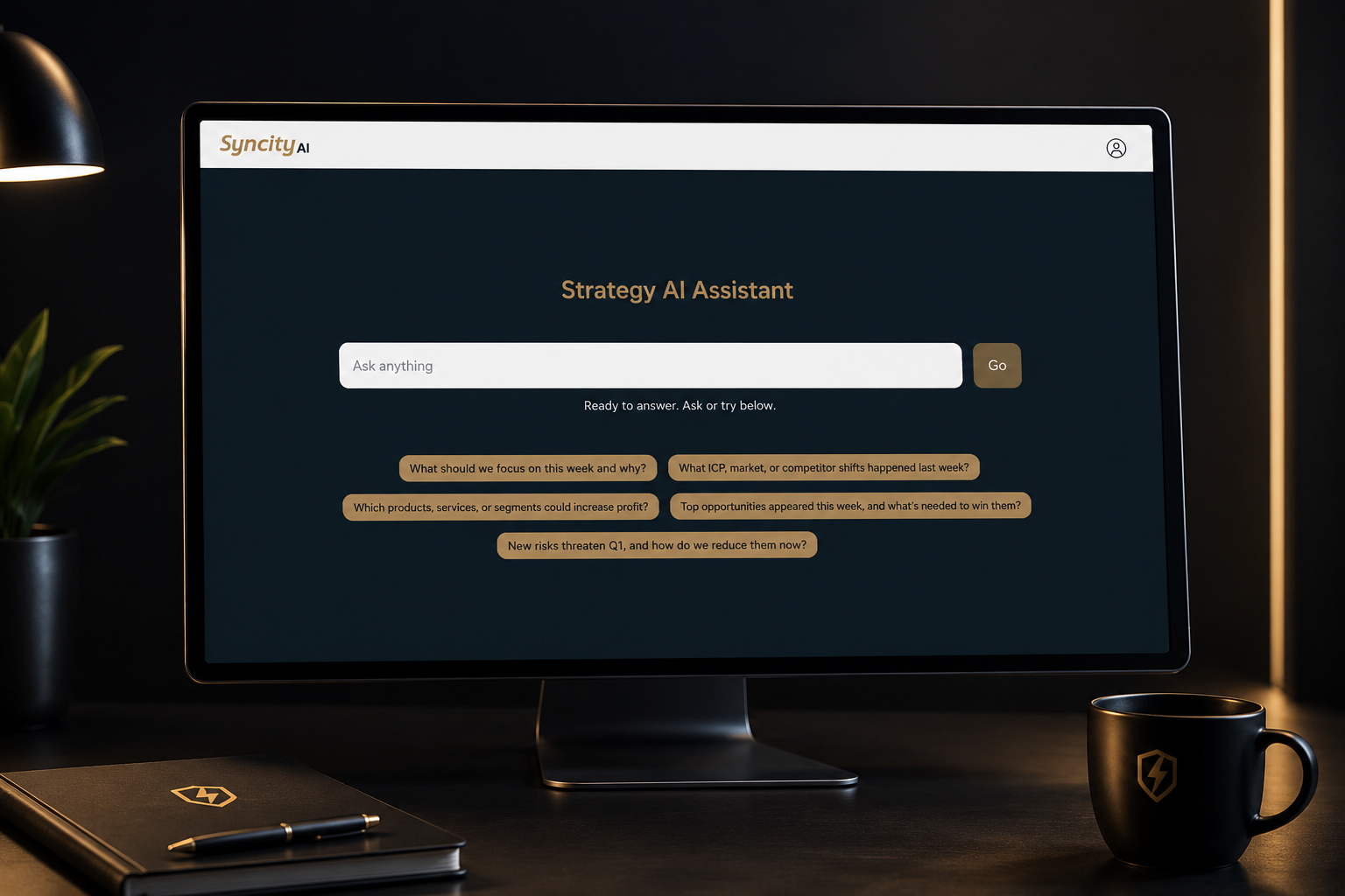 Computer monitor displaying a Strategy AI Assistant interface with a search bar and various suggested questions, a black notebook with a pen, a black coffee mug, and a plant in a black pot on a dark desk.