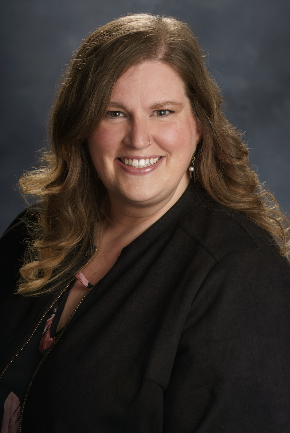 A smiling woman with wavy, light brown hair, wearing a black jacket and pearl earrings. Finance Director at Victory Life Church.