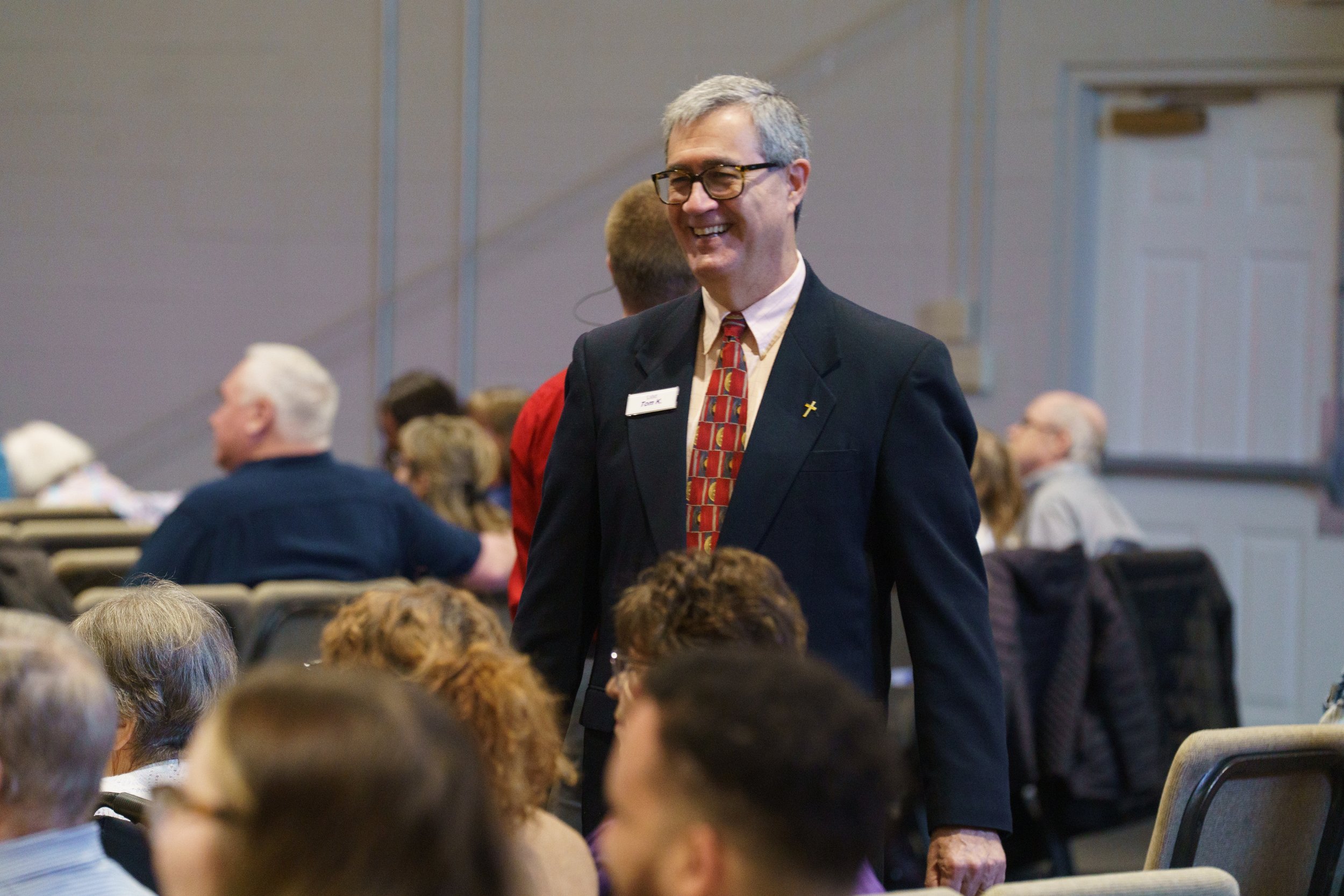 A man in a suit with glasses and a tie smiling and engaging as an usher at Victory Life Church in Stow, OH.