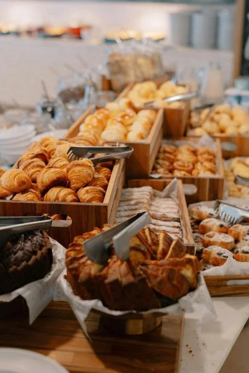 An assortment of baked goods including croissants, danishes, and bread slices arranged on a buffet table.