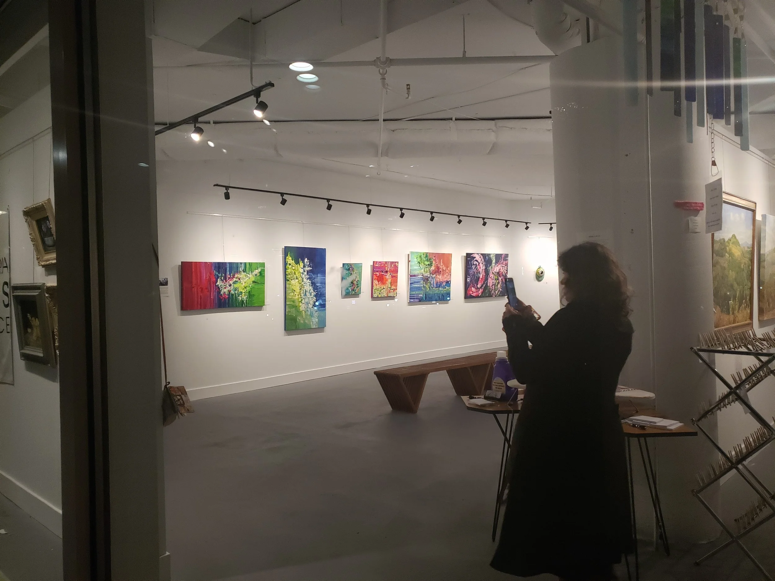 Person taking a photo of colorful abstract paintings in an art gallery