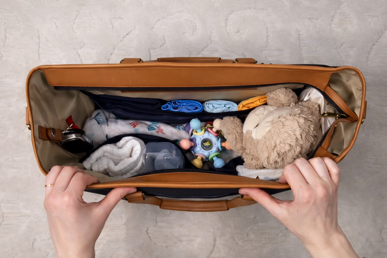 Open diaper bag containing baby clothes, a plush toy, a teething ring, a water bottle, and other baby essentials.