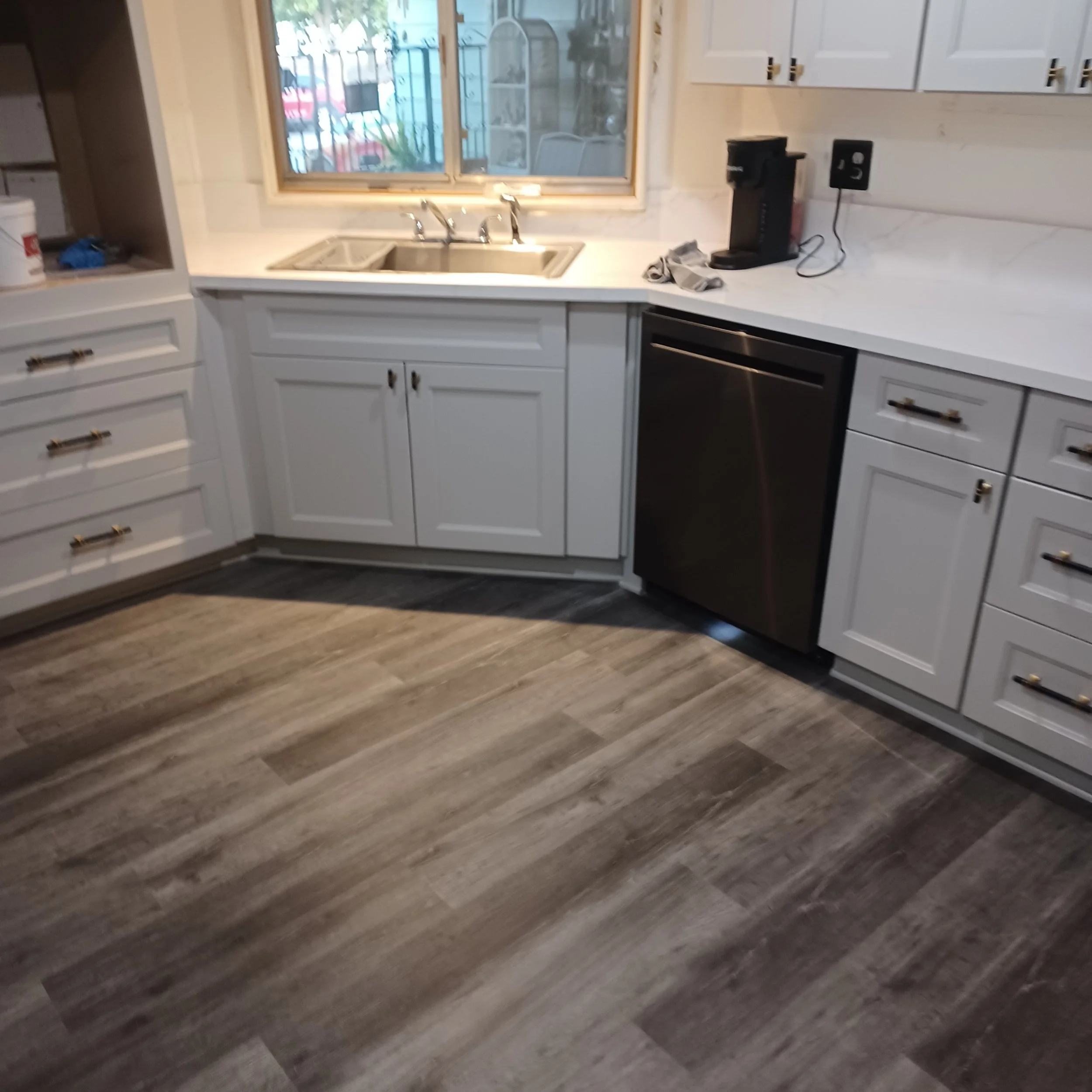 A kitchen with white cabinets, a stainless steel double sink under a window, a black coffee maker, and a countertop with a towel and electrical outlet.