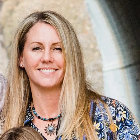 Smiling woman with long blonde hair wearing a floral shirt and layered necklaces