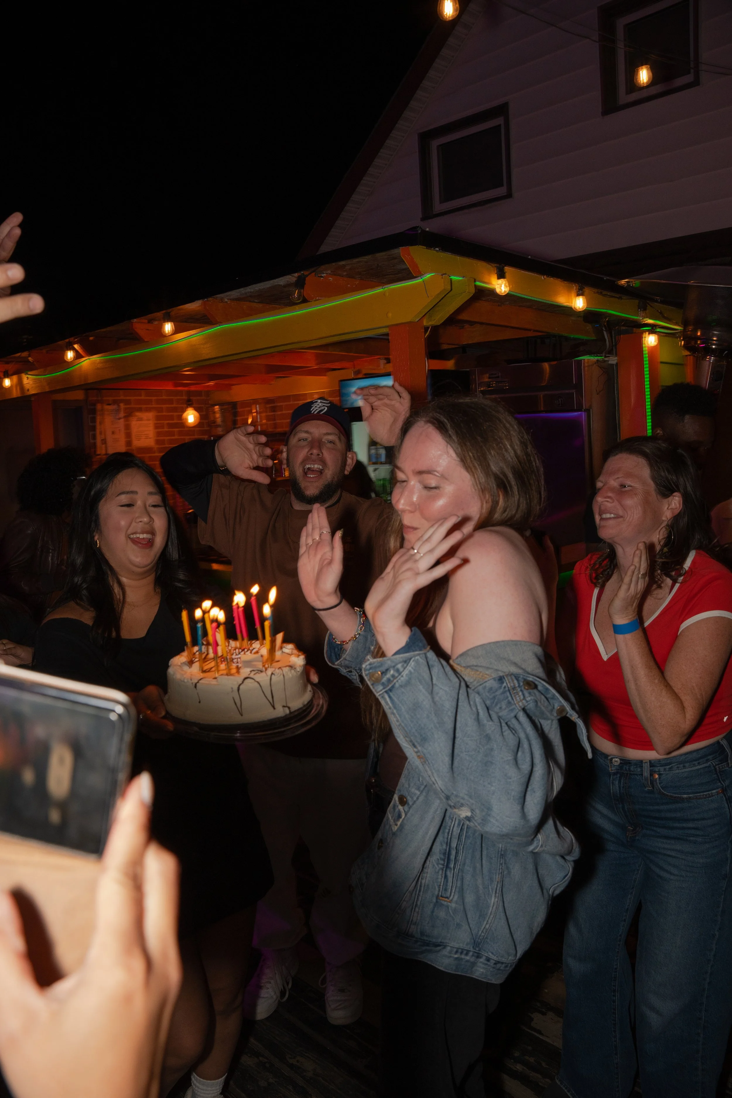 People celebrating birthday with a cake topped with lit candles in a lively party setting