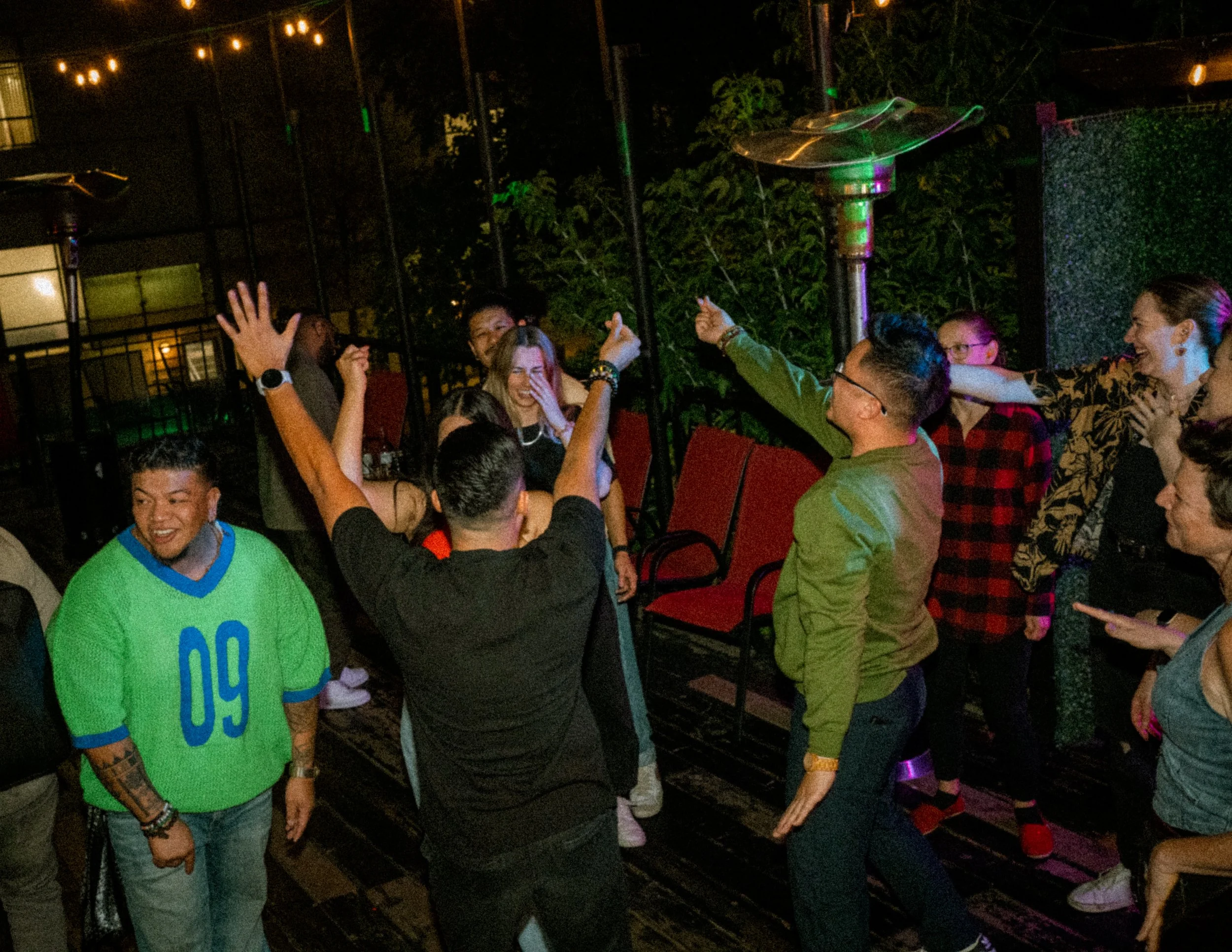 Group of people dancing and celebrating in a dimly lit outdoor space at night.