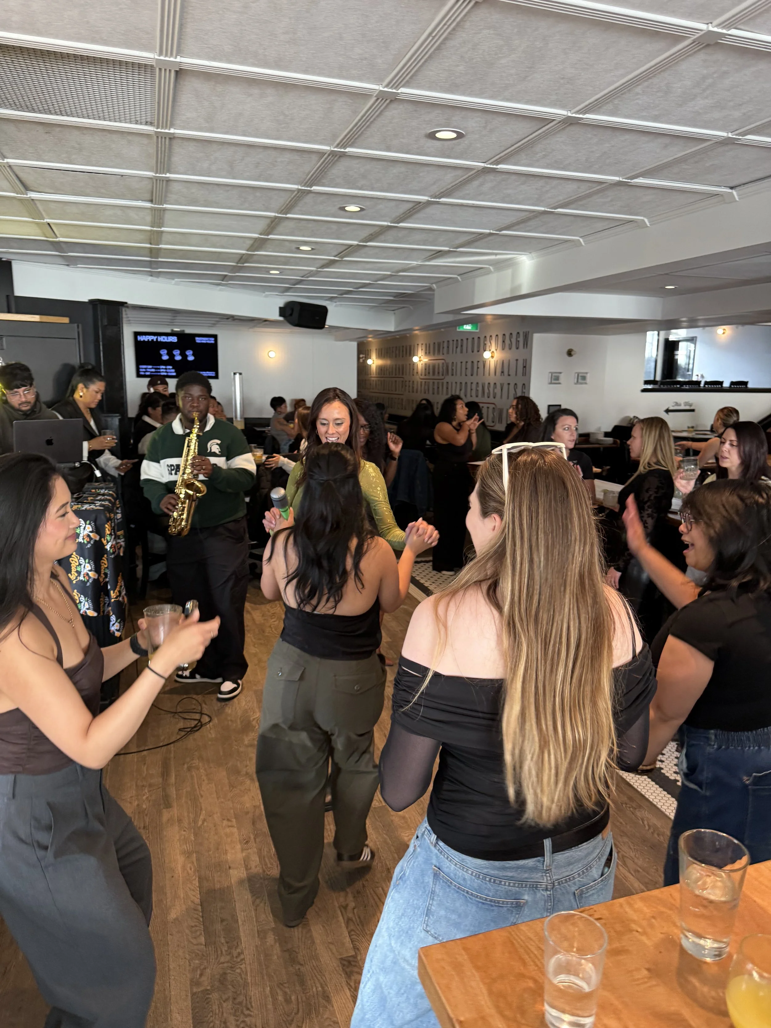 People dancing and enjoying music in a lively indoor bar or restaurant with a live musician playing saxophone.