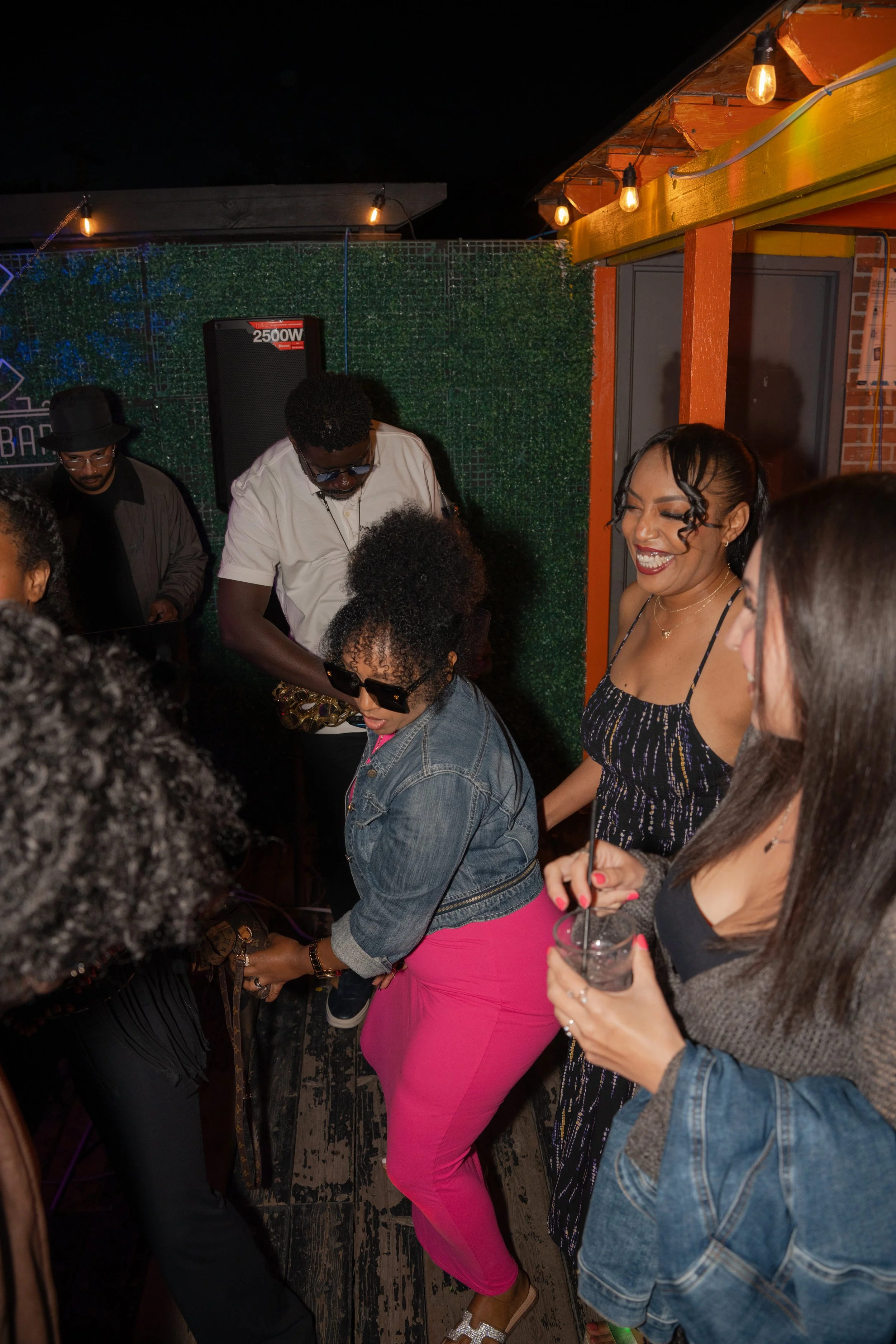 People dancing and socializing at a night party with string lights indoors.