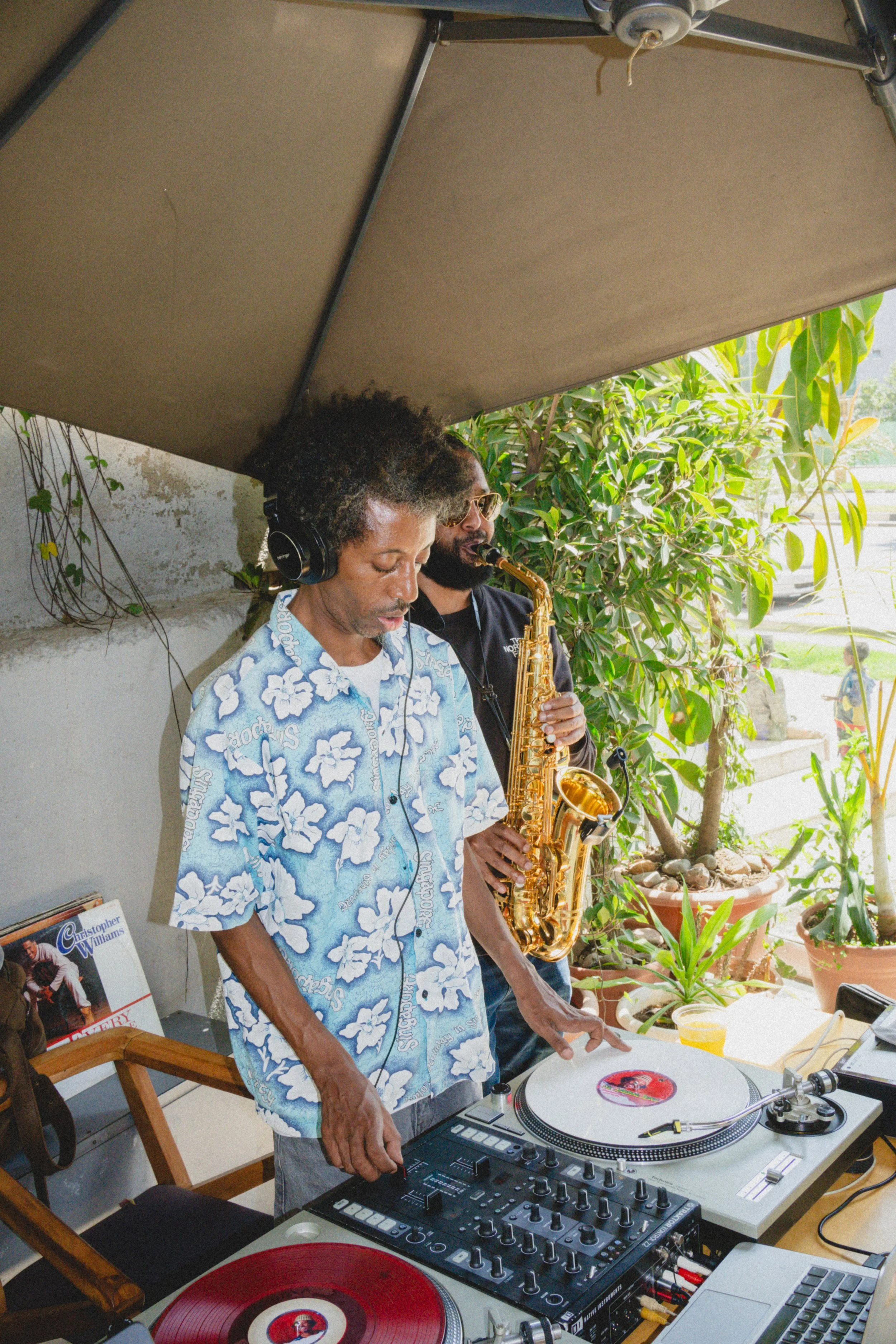 Two musicians, one playing a saxophone and the other a DJ, performing outdoors.